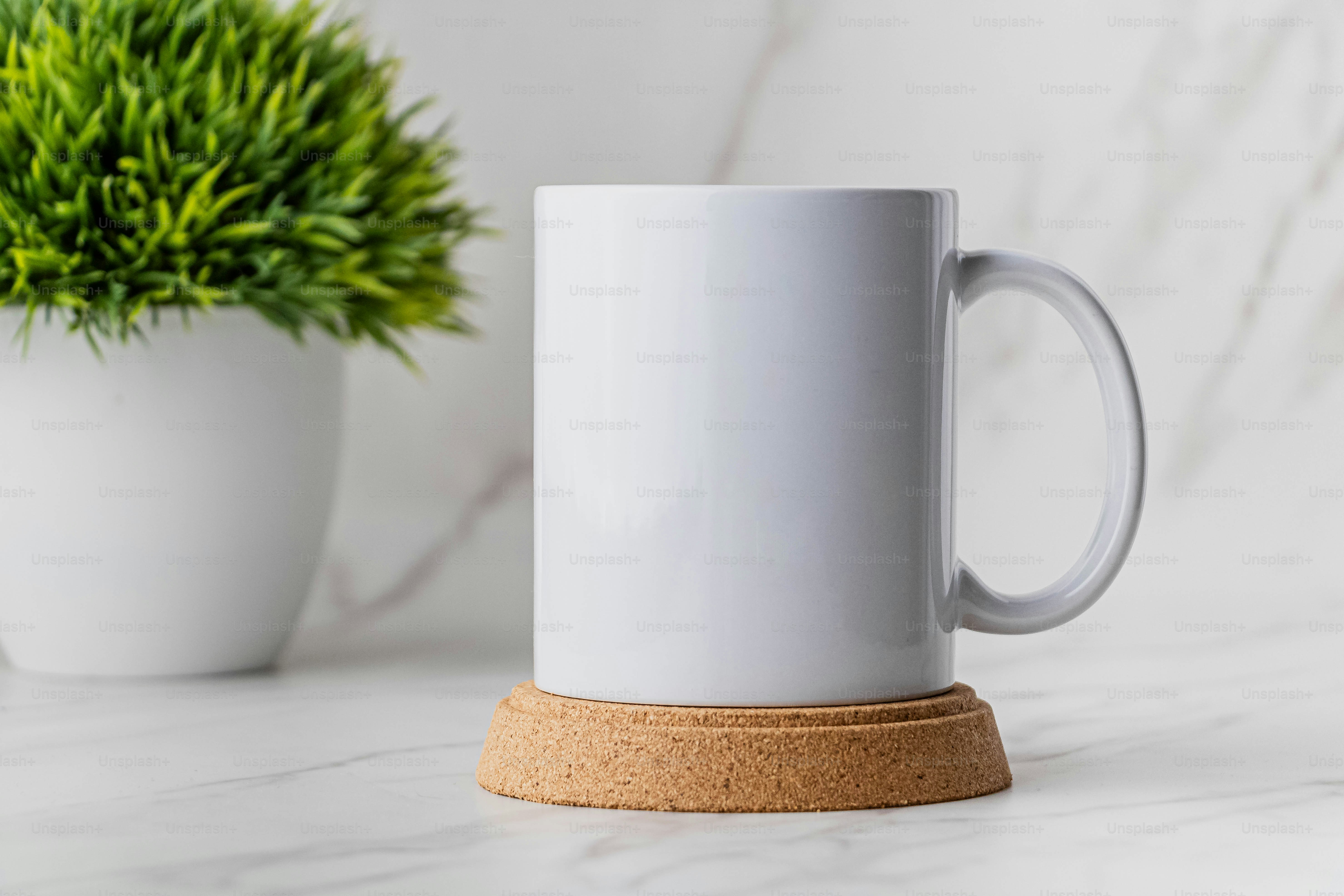 A white coffee mug sitting on top of a counter next to a potted plant