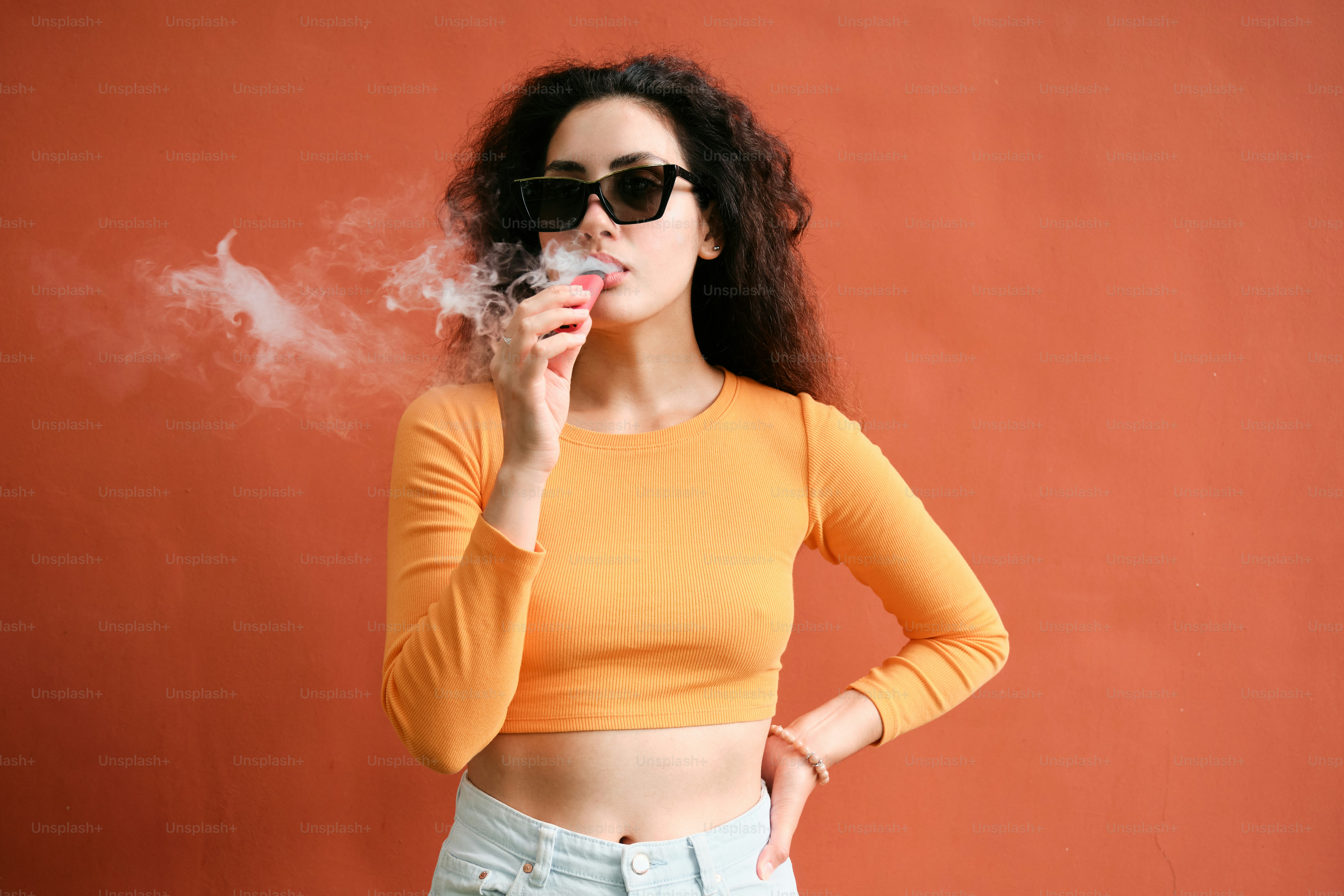 A woman smoking a cigarette in front of a red wall