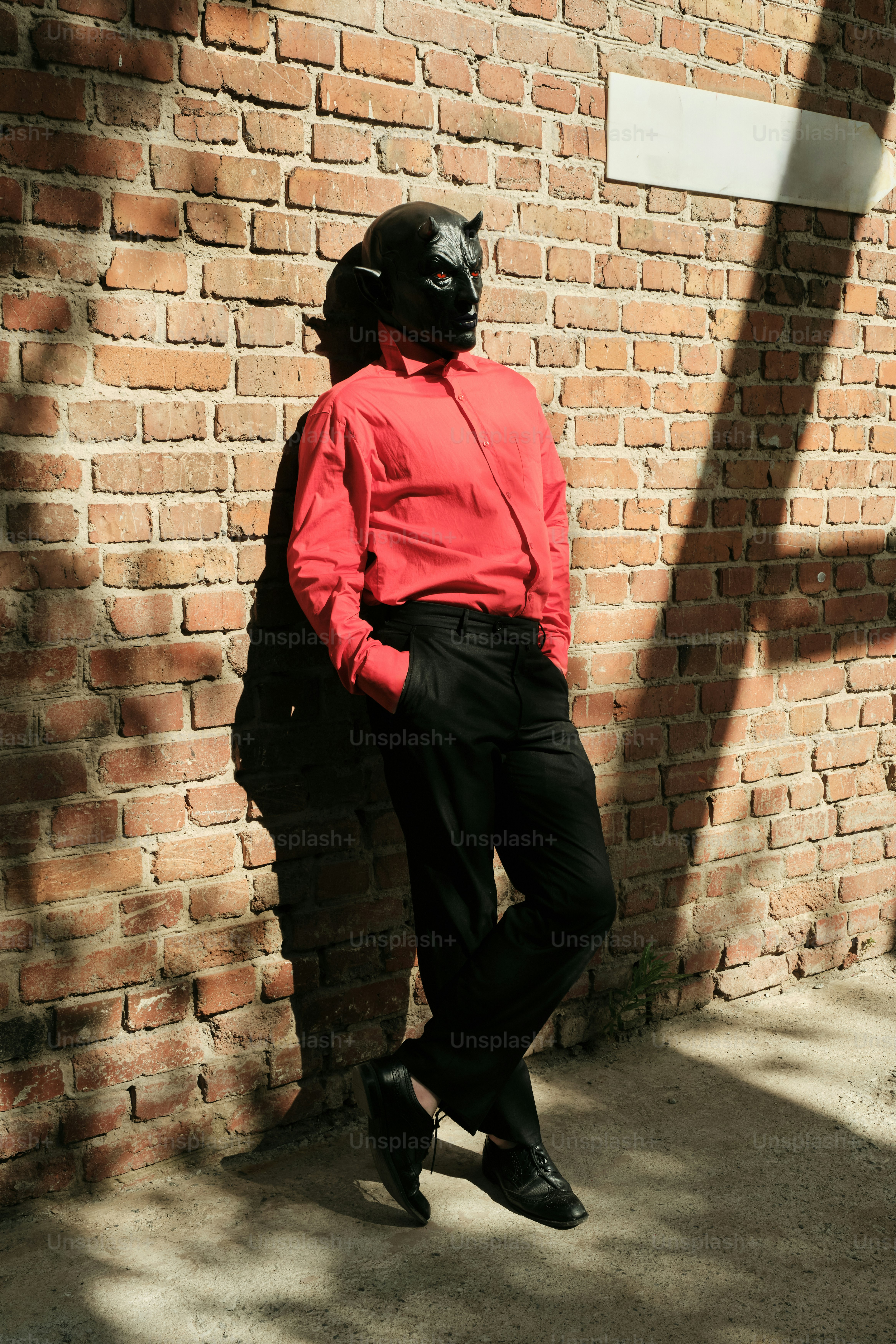 A man in a red shirt and black pants leaning against a brick wall