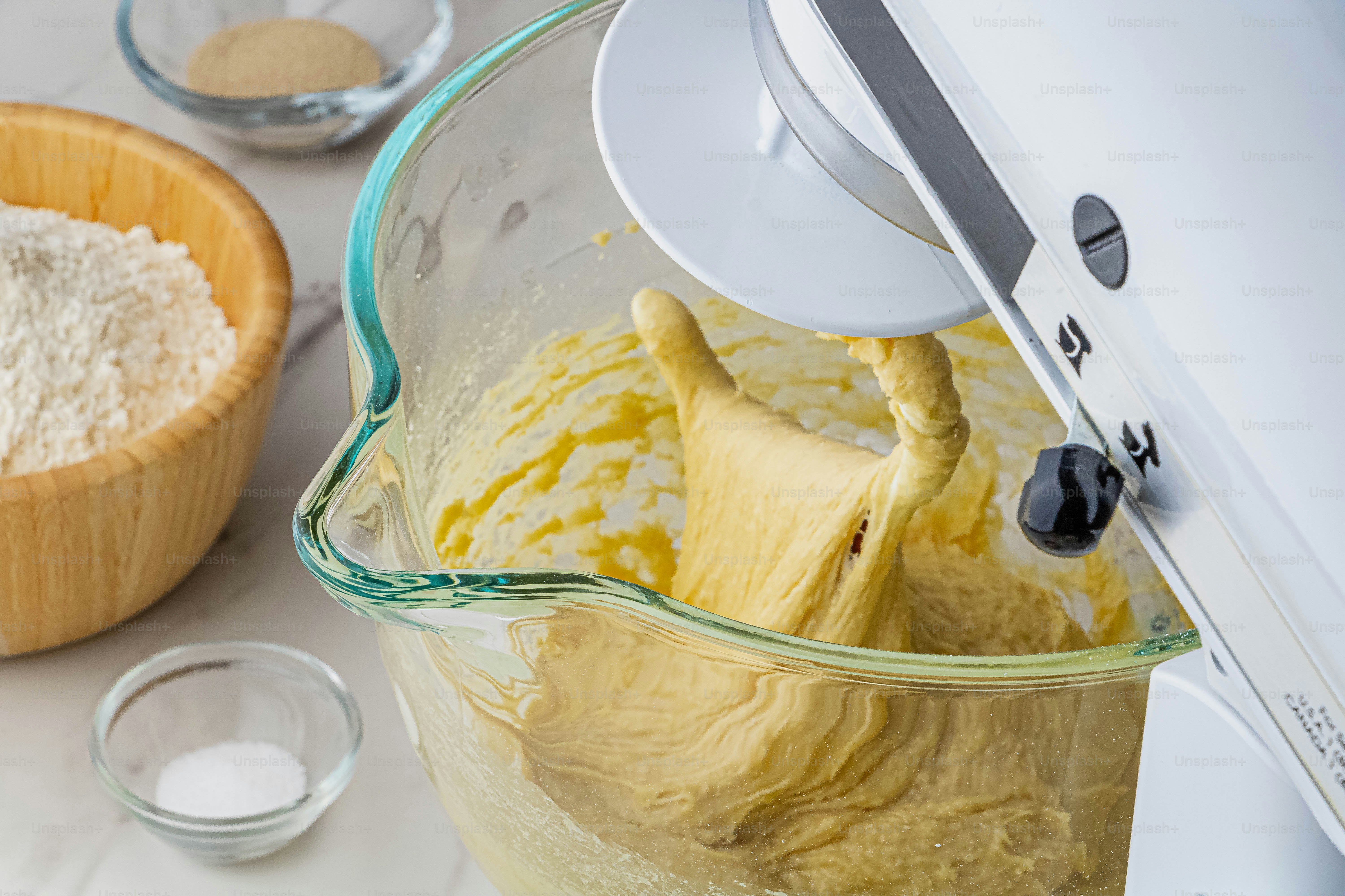Ein mit Teig gefüllter Mixer neben einer Schüssel mit Mehl
