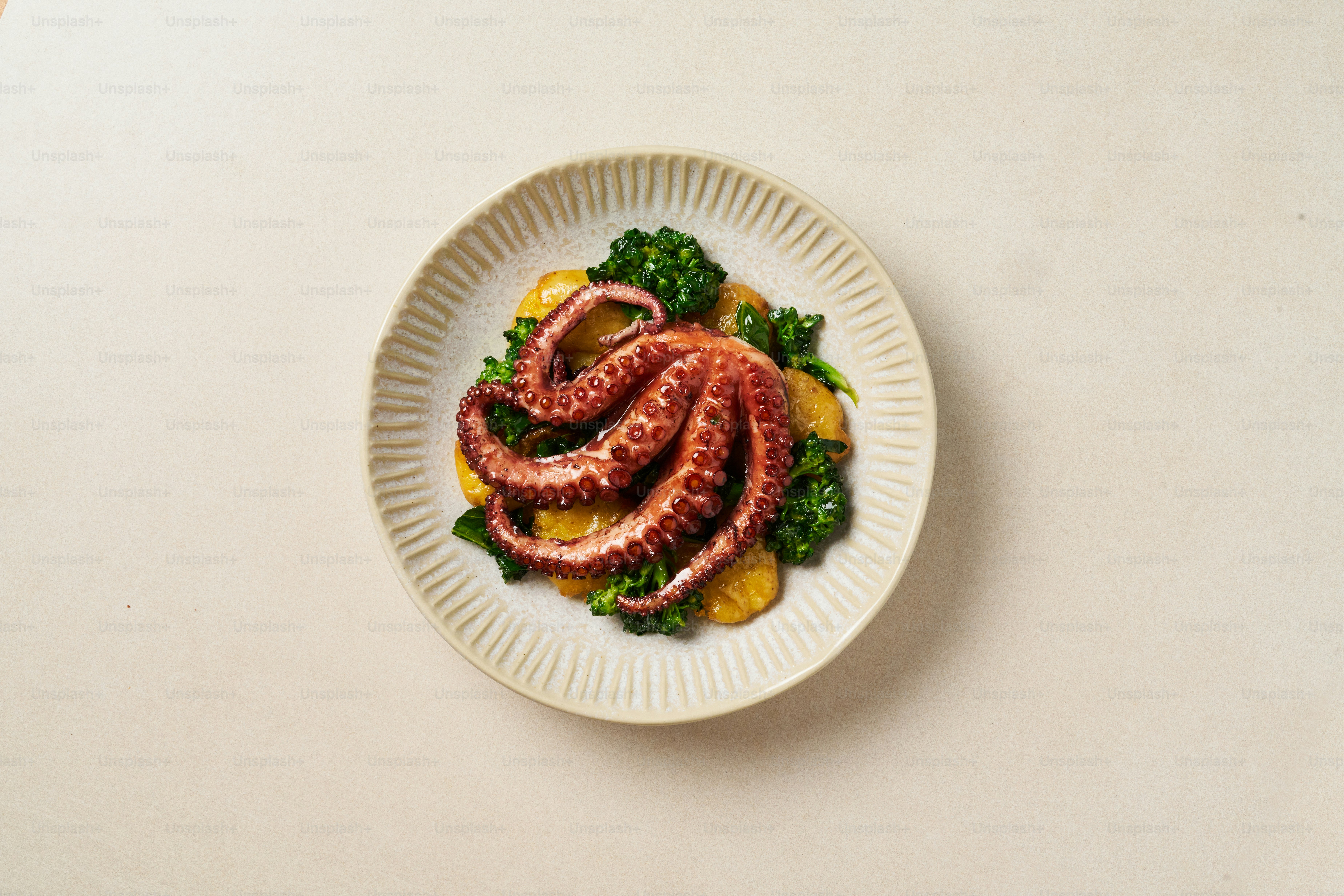 A white plate topped with an octopus on top of greens