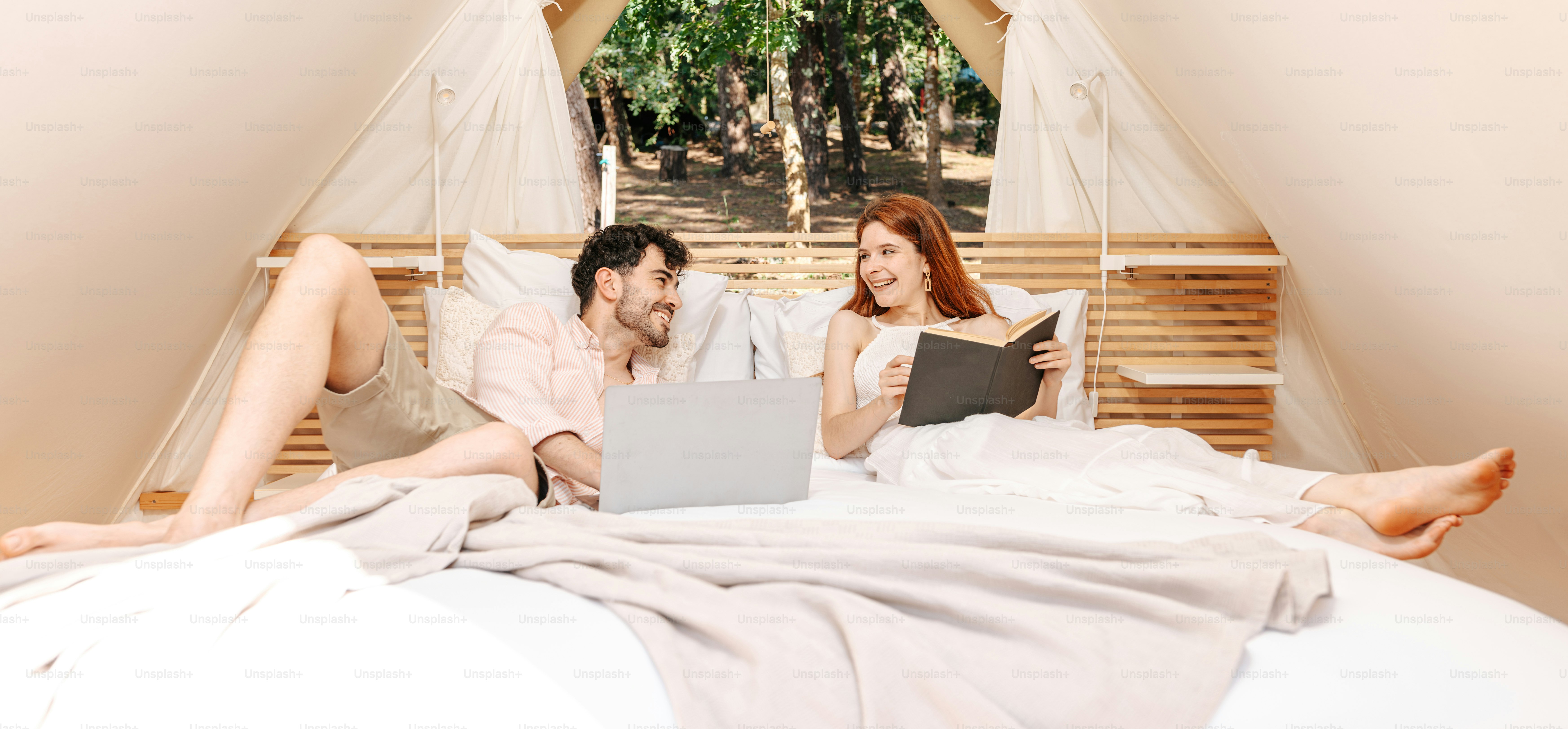 A man and a woman sitting on a bed looking at a laptop