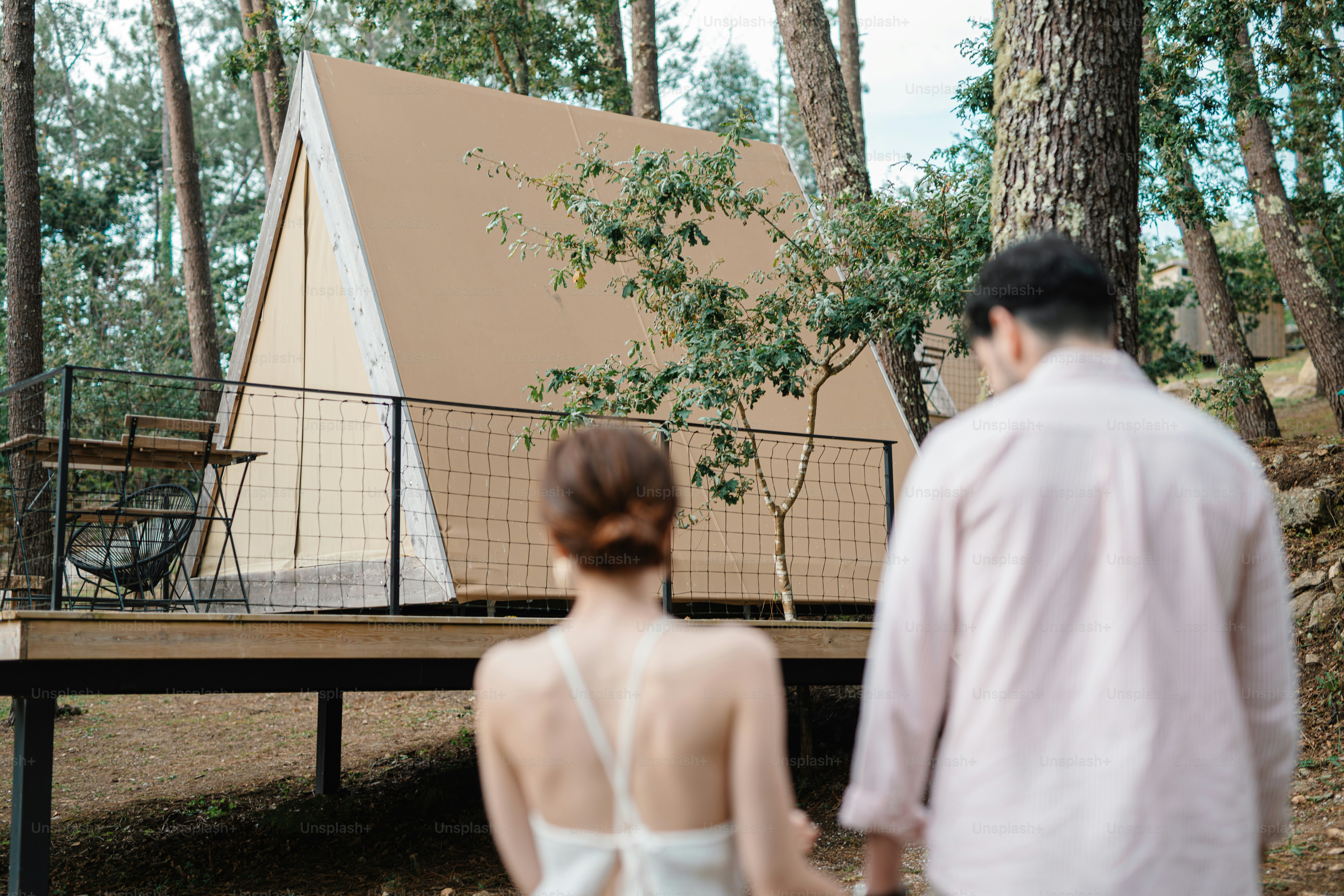 A man and a woman standing in front of a tent in the woods