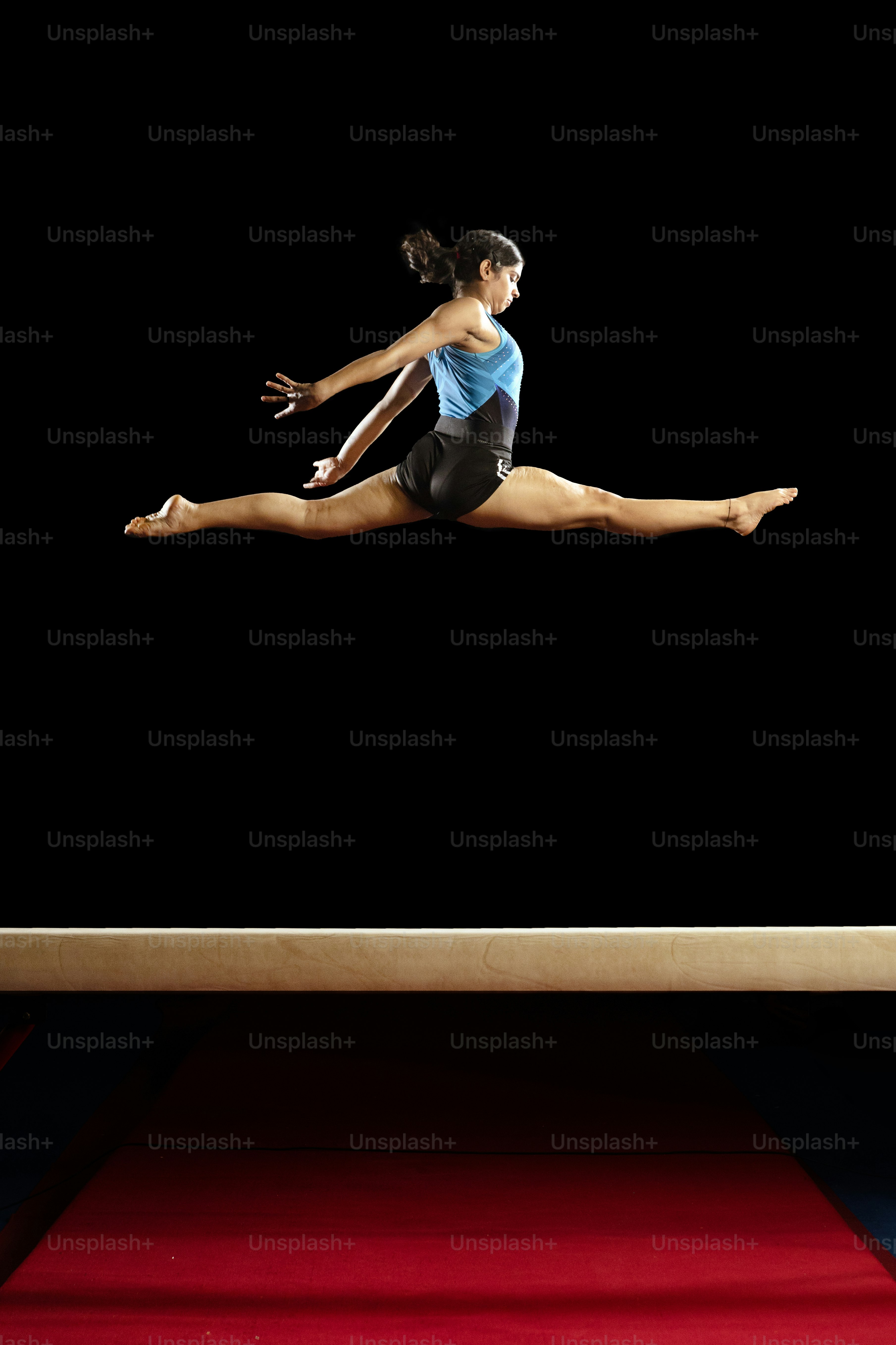 A woman in a blue shirt and black shorts is doing a trick on a beam