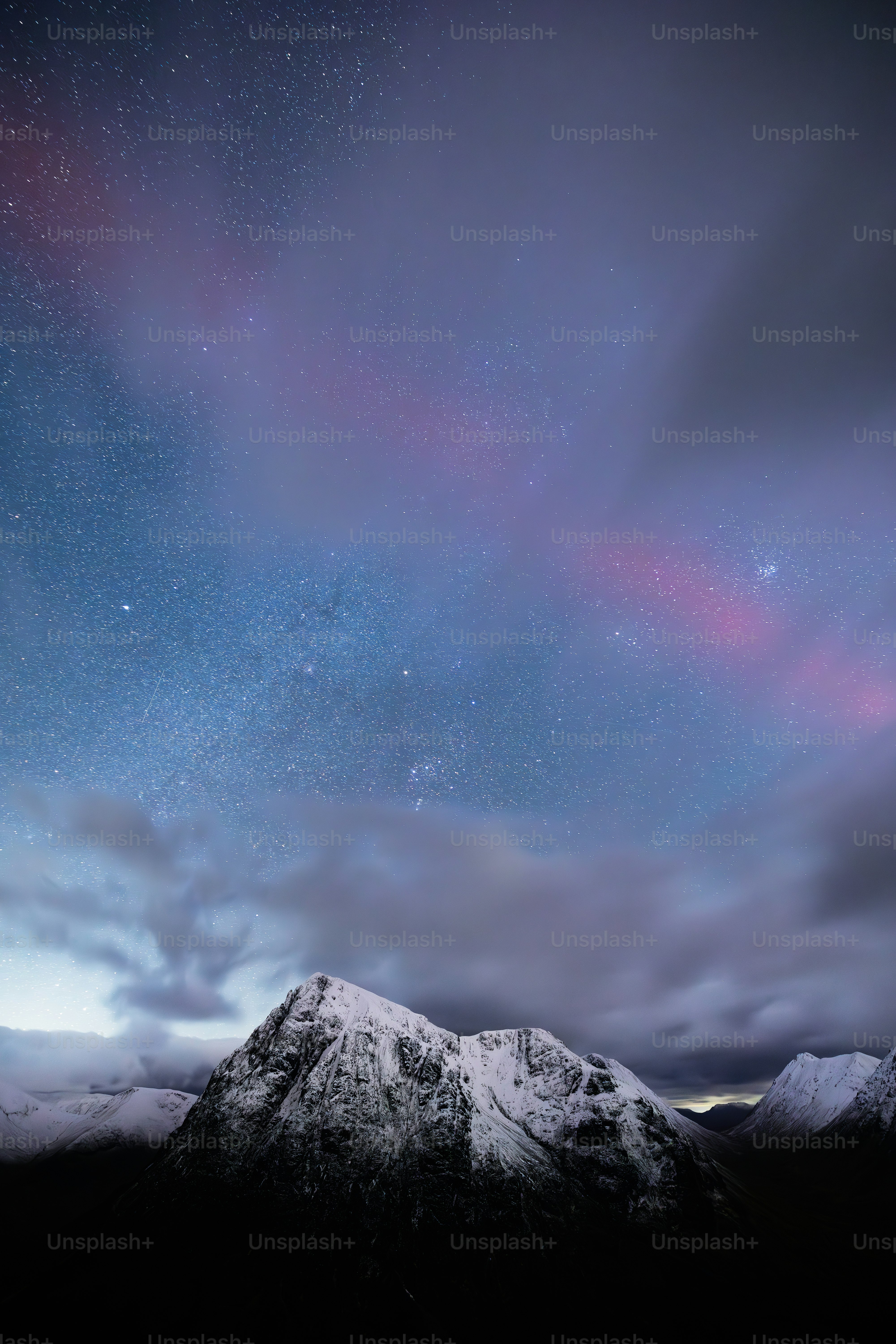 A night sky with stars and clouds over a mountain range