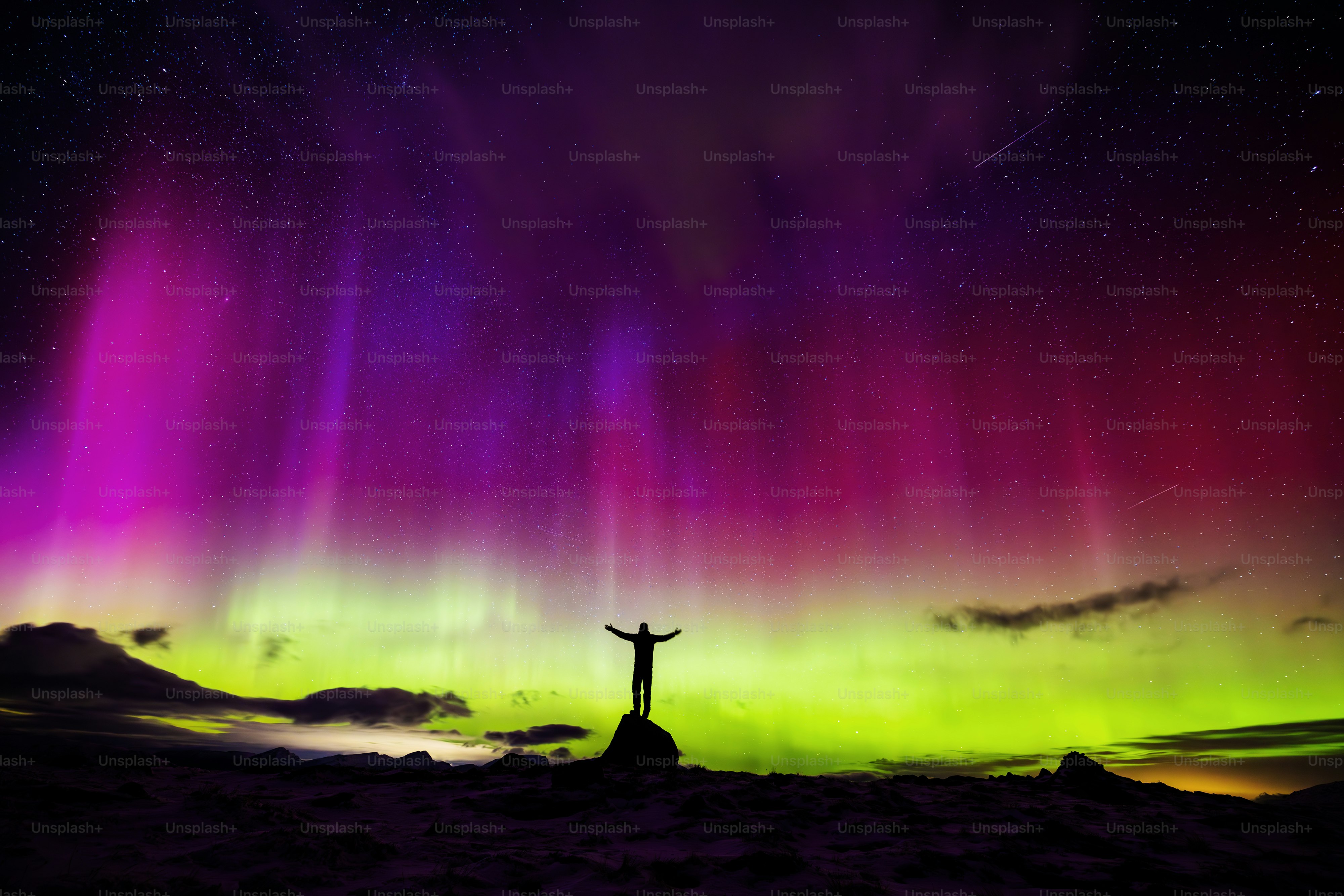 A person standing on top of a hill under a purple and green sky