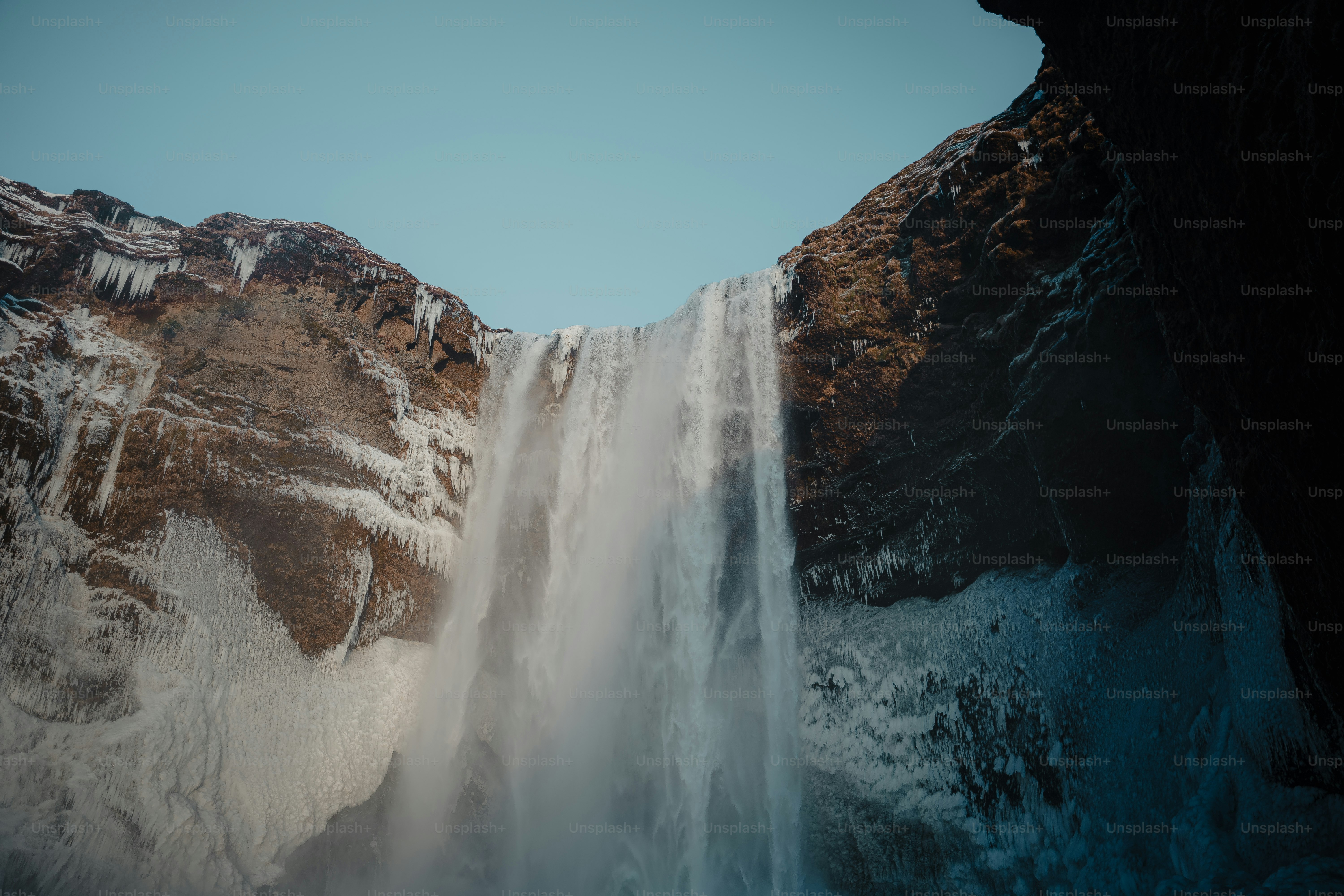 A large waterfall with snow on the side of it photo – Iceland Image on ...