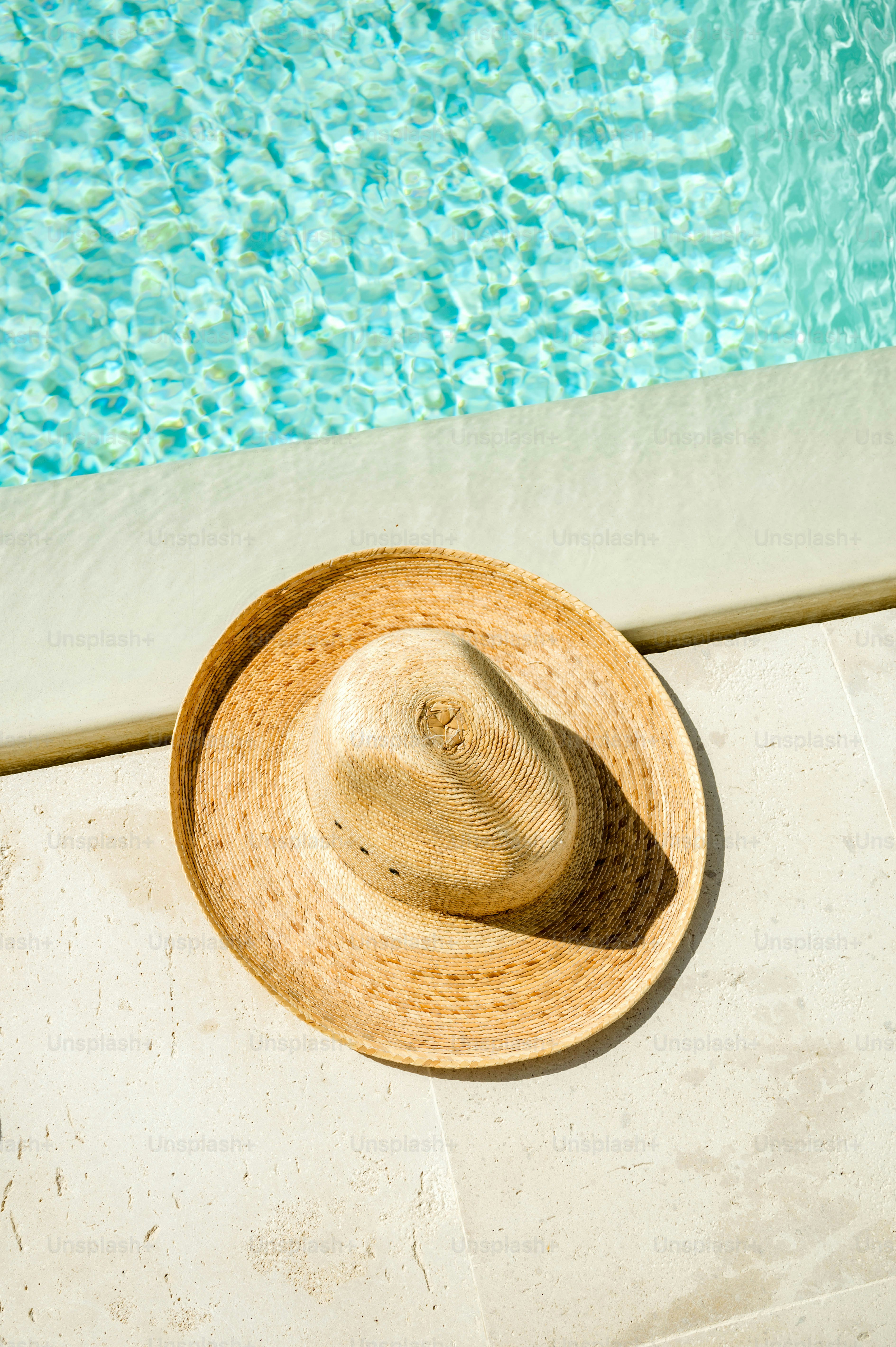 A straw hat sitting on the edge of a swimming pool