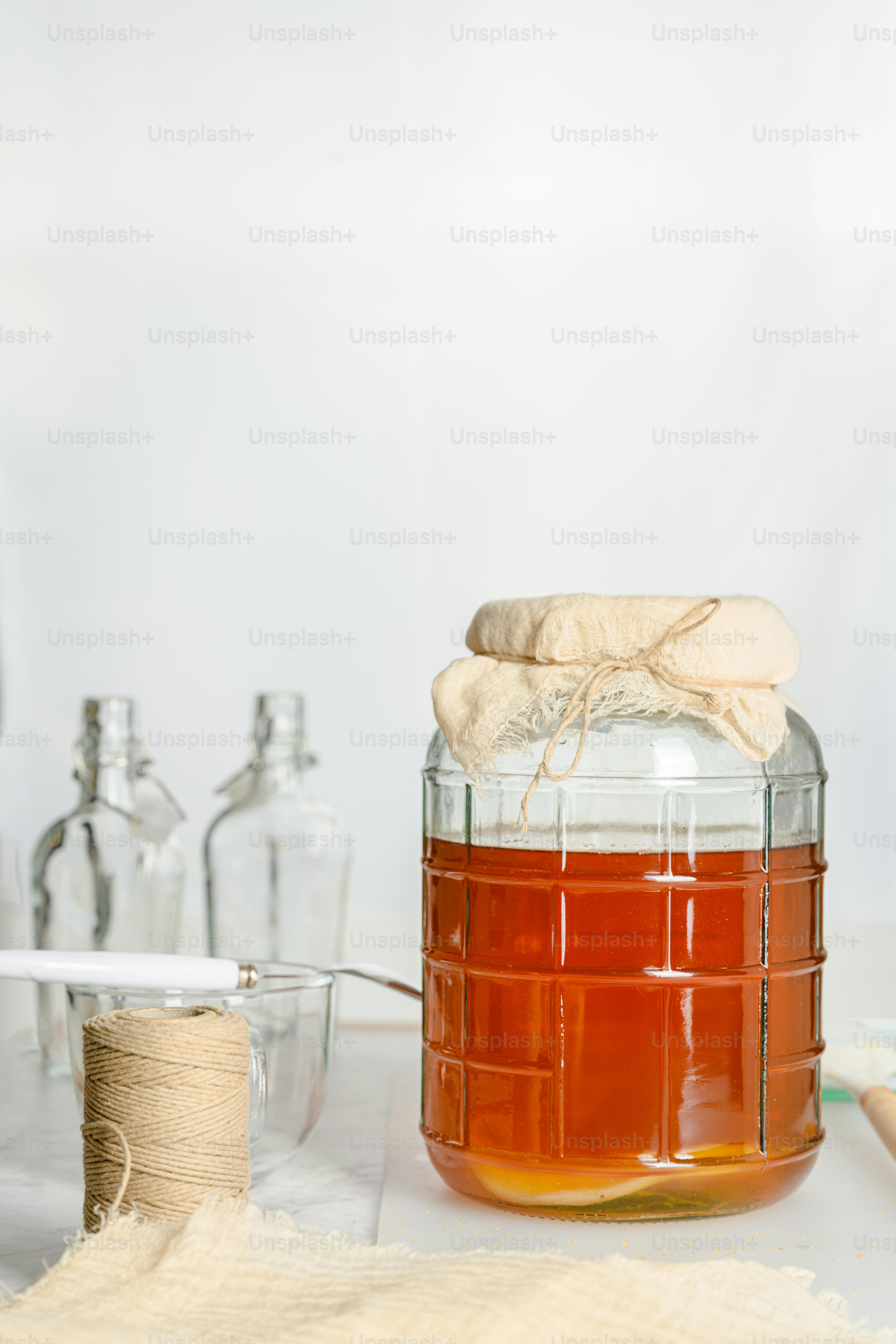 A jar of honey sits on a table next to a spool of twine