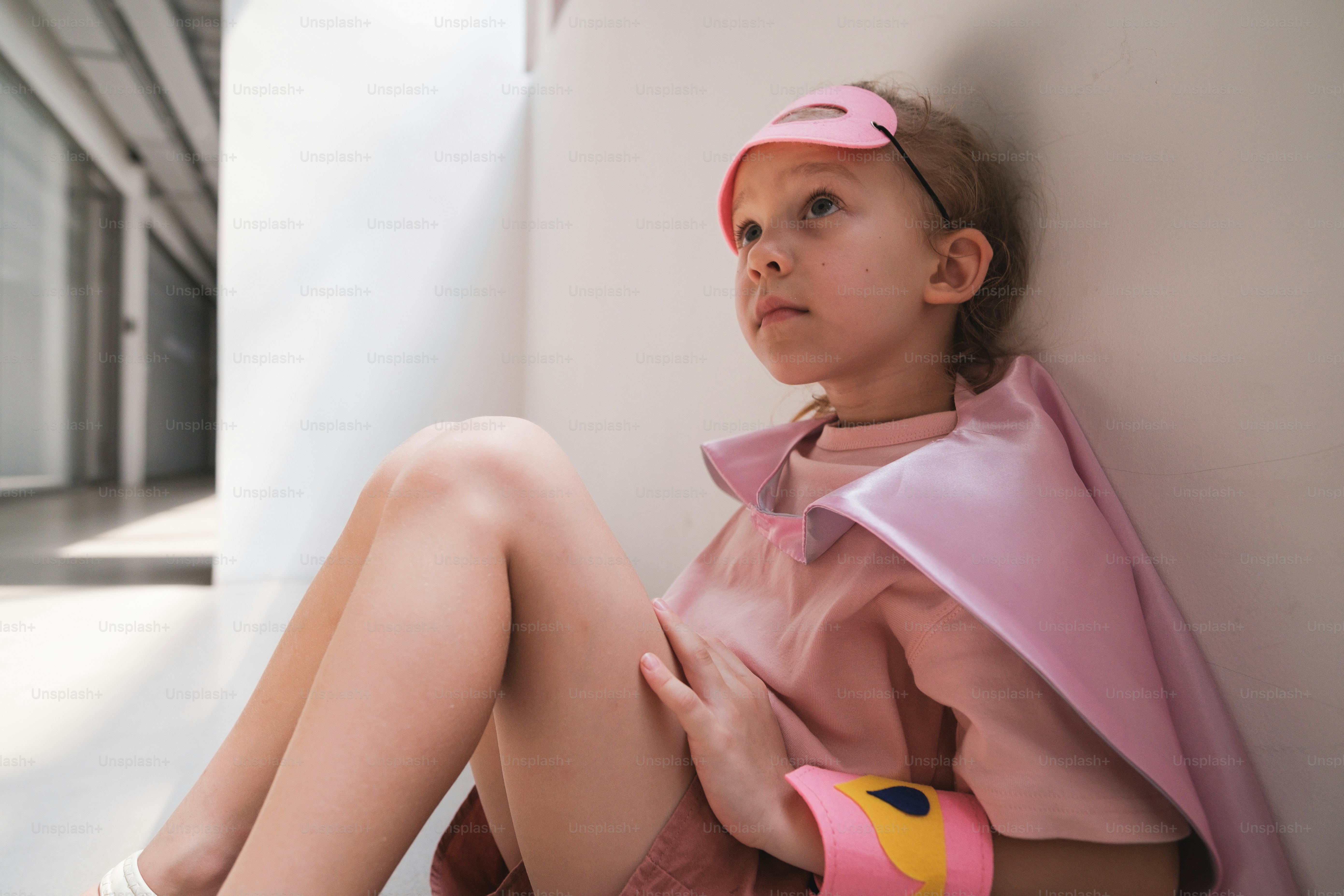 A little girl sitting on the floor with a pink coat over her head