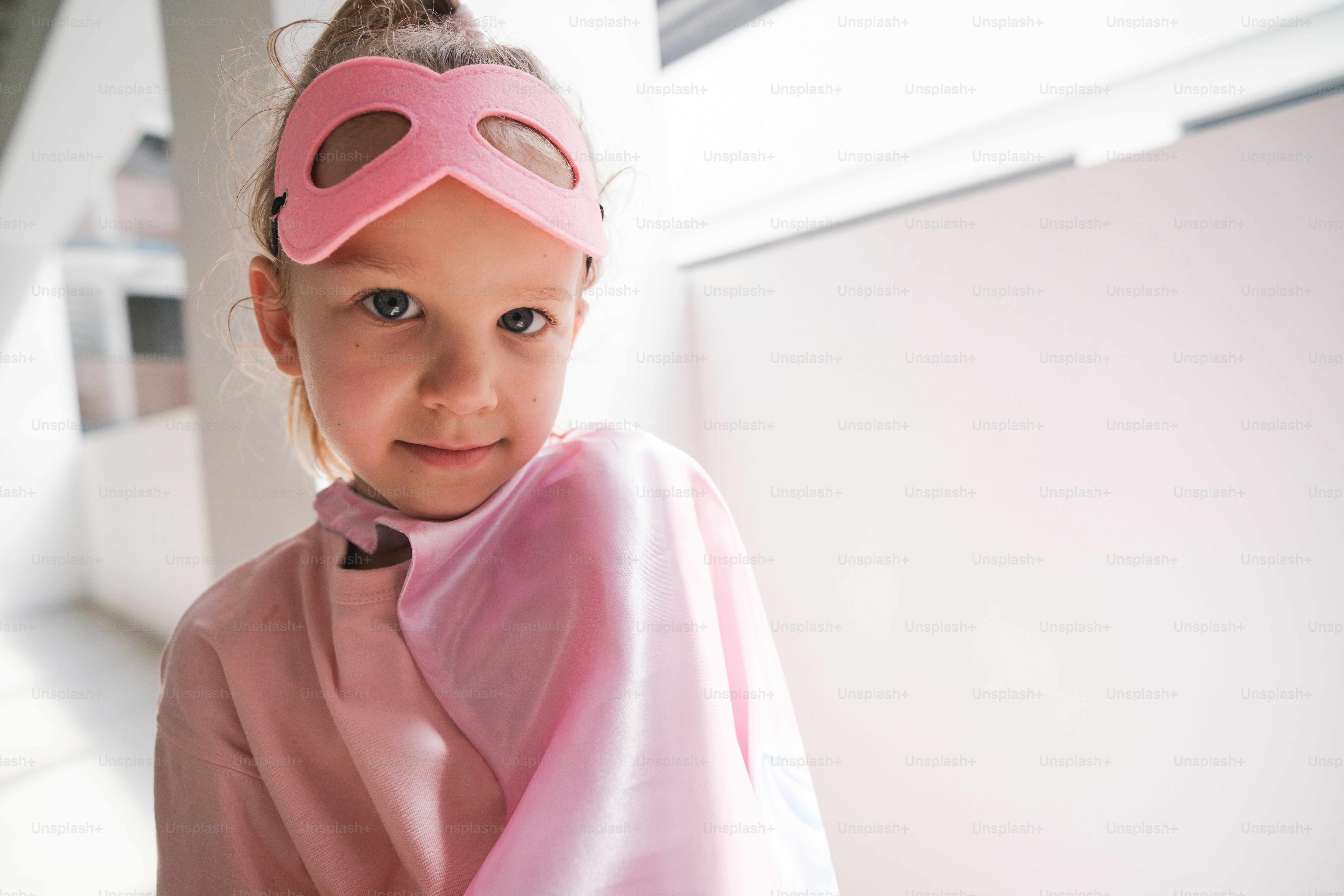 A little girl wearing a pink mask and a pink cape