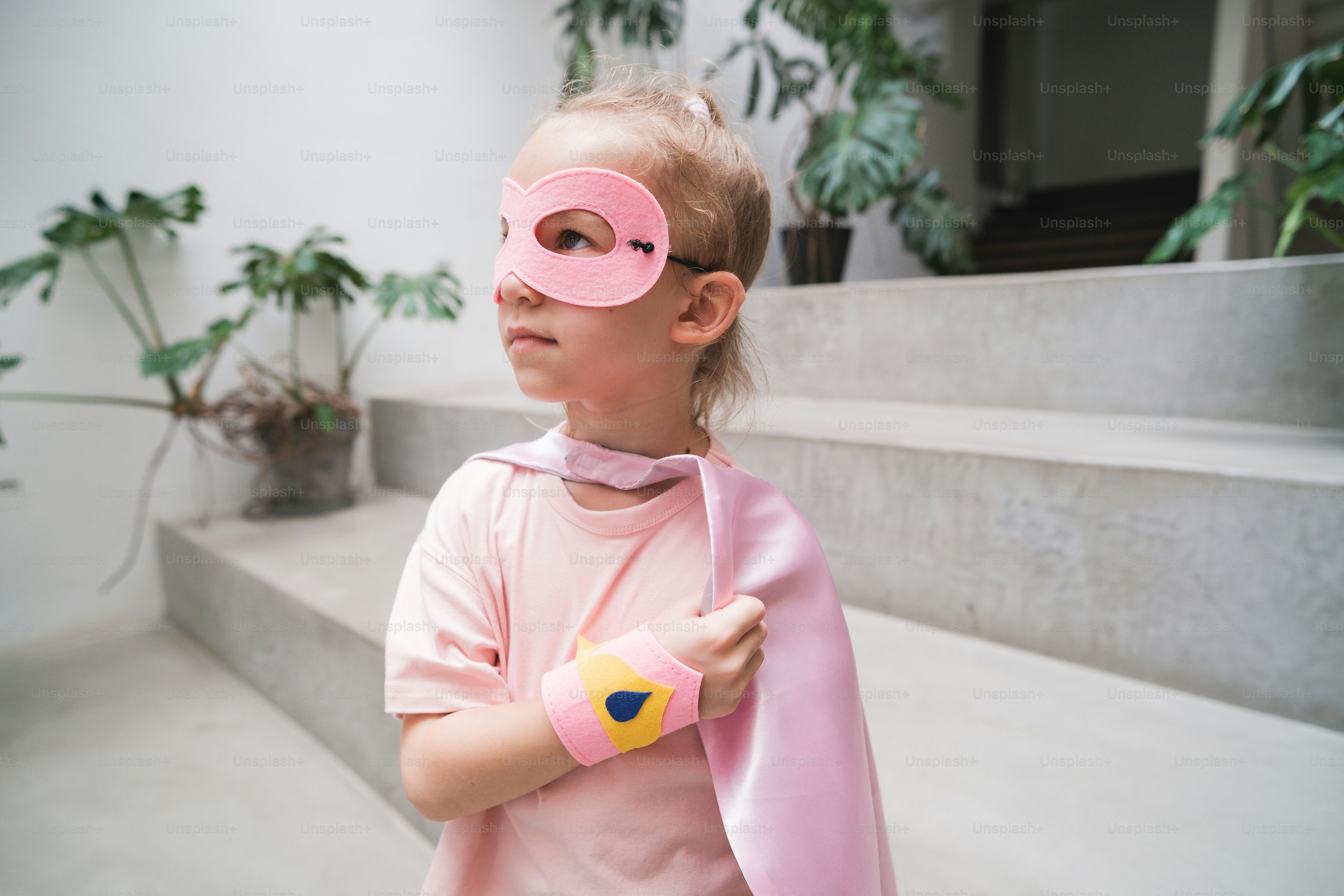 A little girl wearing a pink mask and a pink scarf