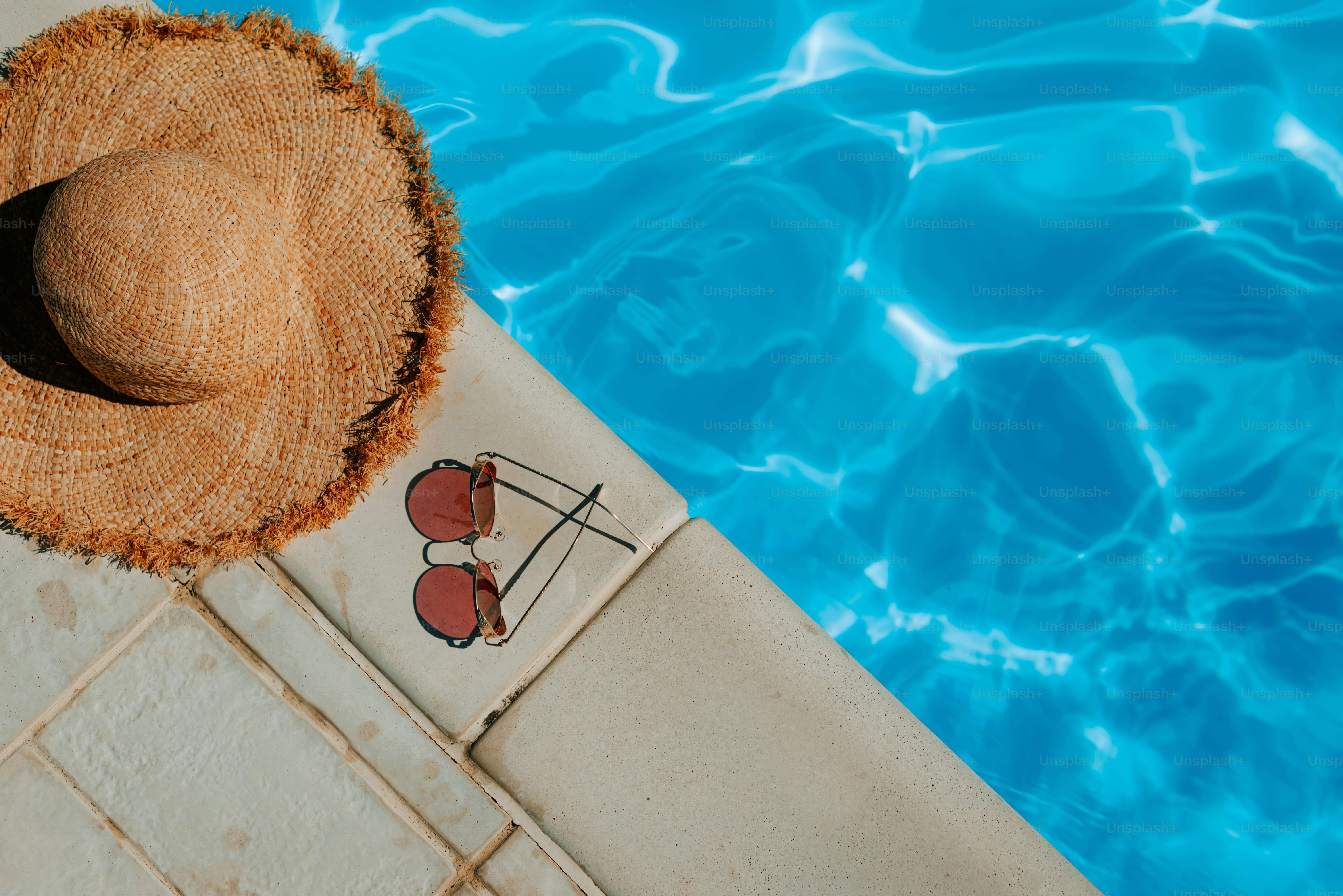 A straw hat sitting on top of a tiled floor next to a swimming pool ...