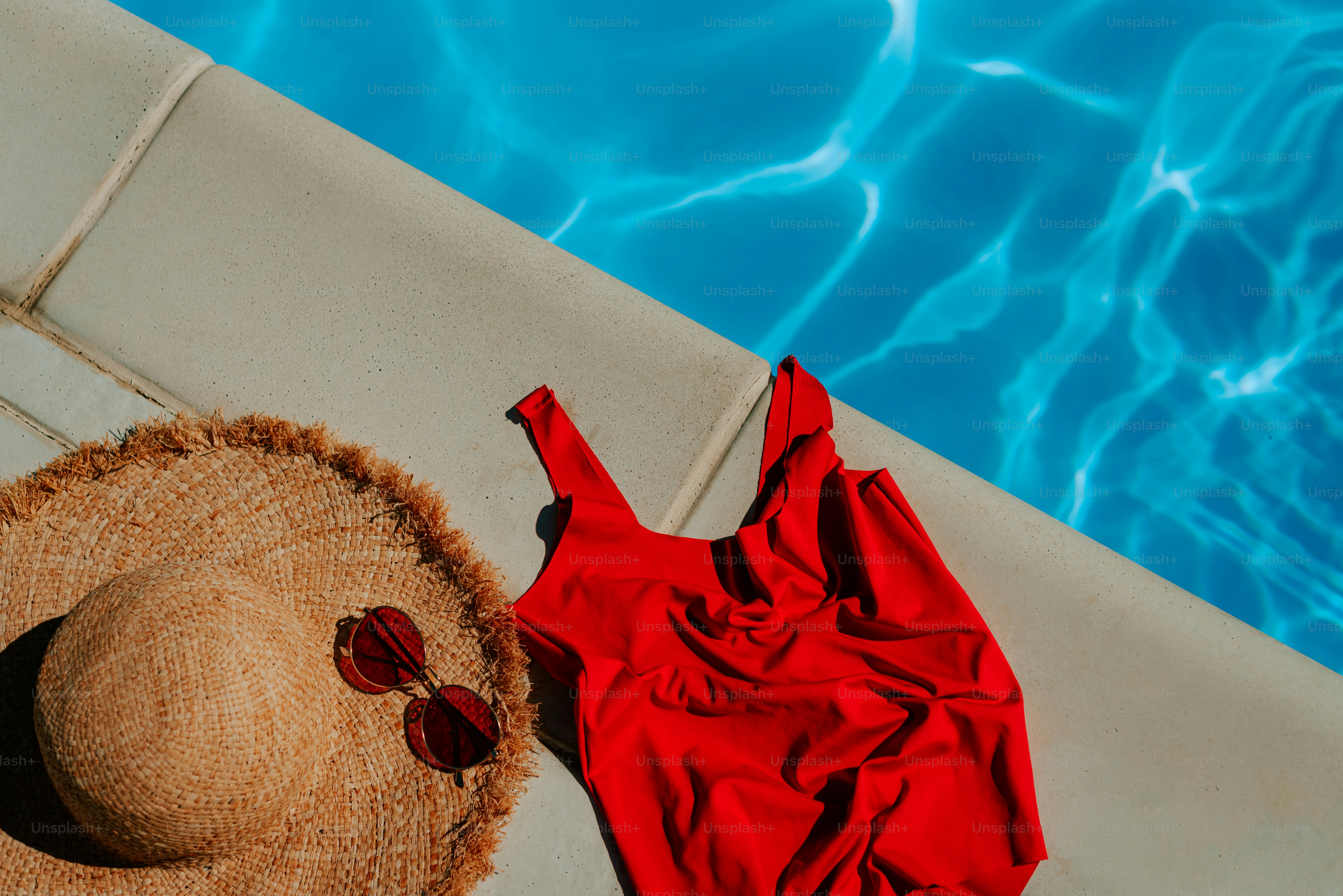 A straw hat and a red swimsuit by a swimming pool