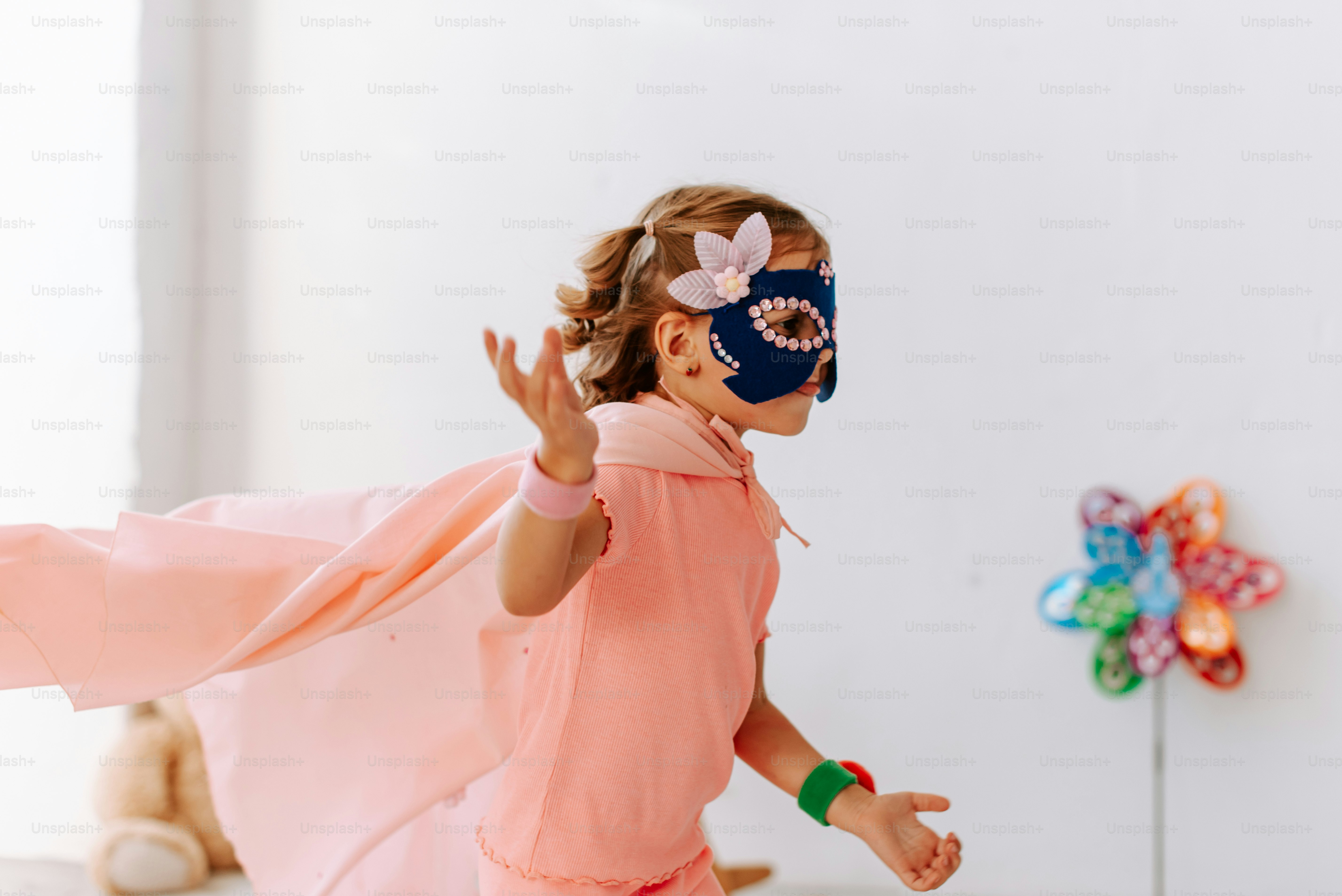 A little girl wearing a mask and pink dress