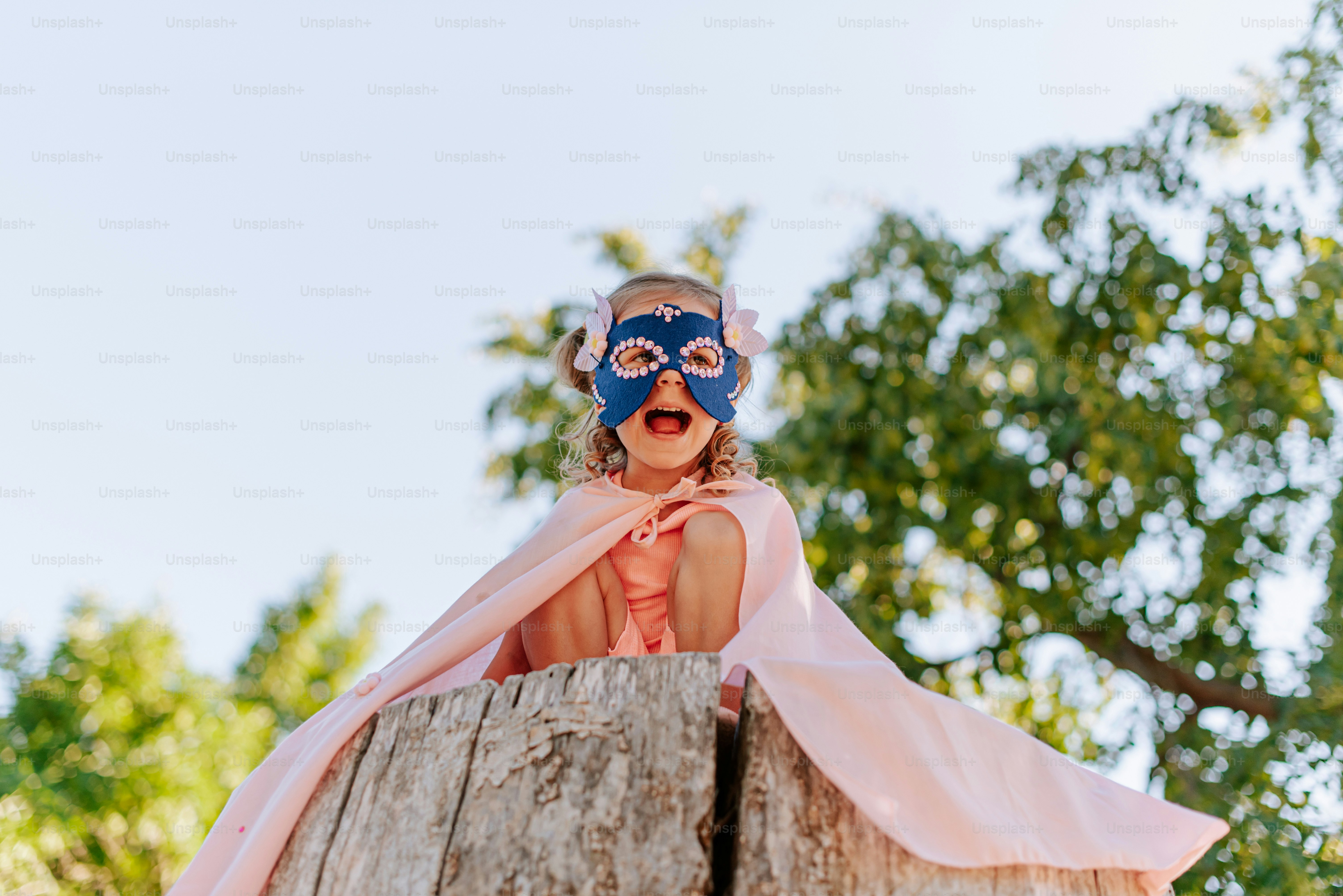 A little girl wearing a mask sitting on top of a tree stump