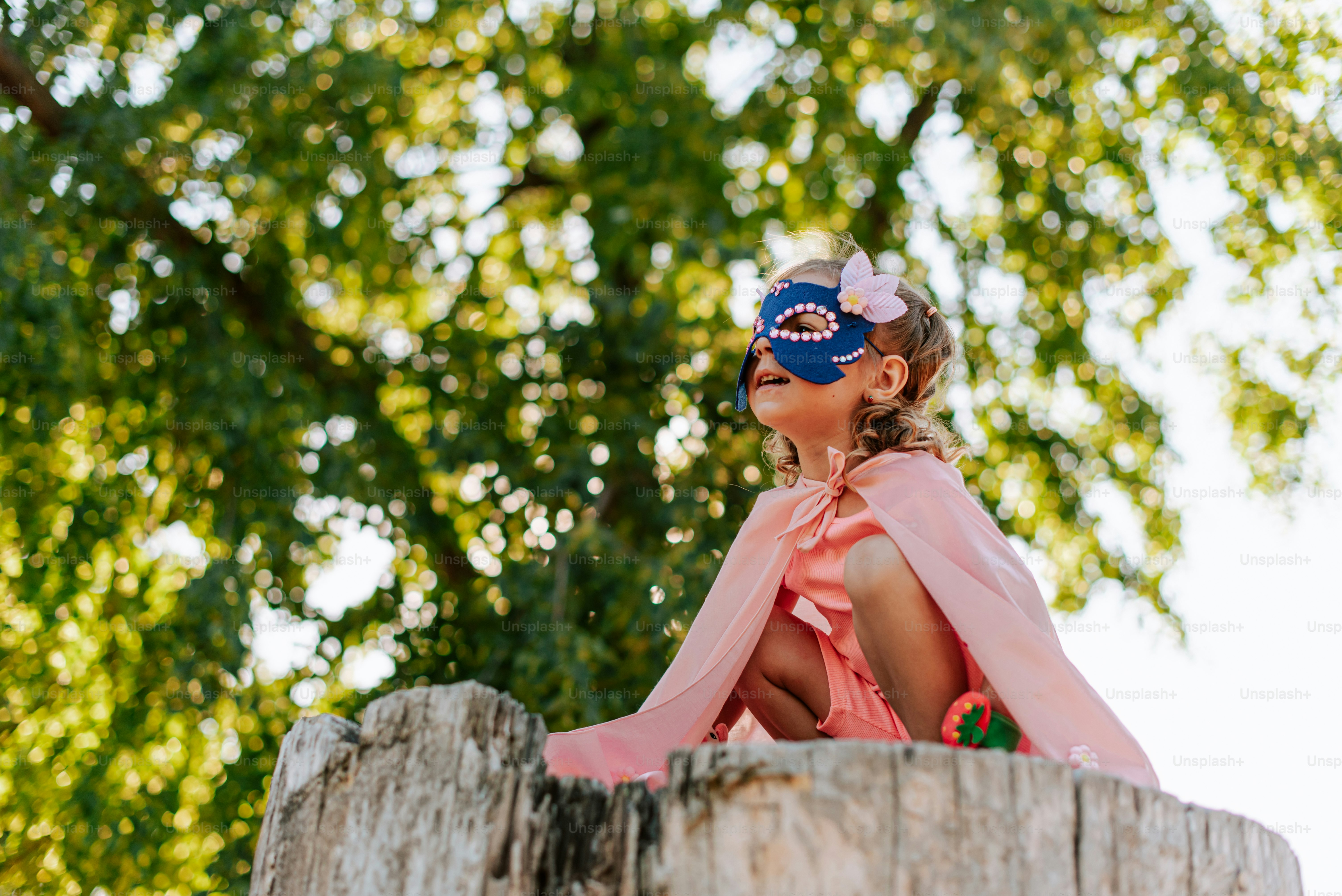 A little girl wearing a mask sitting on top of a tree stump