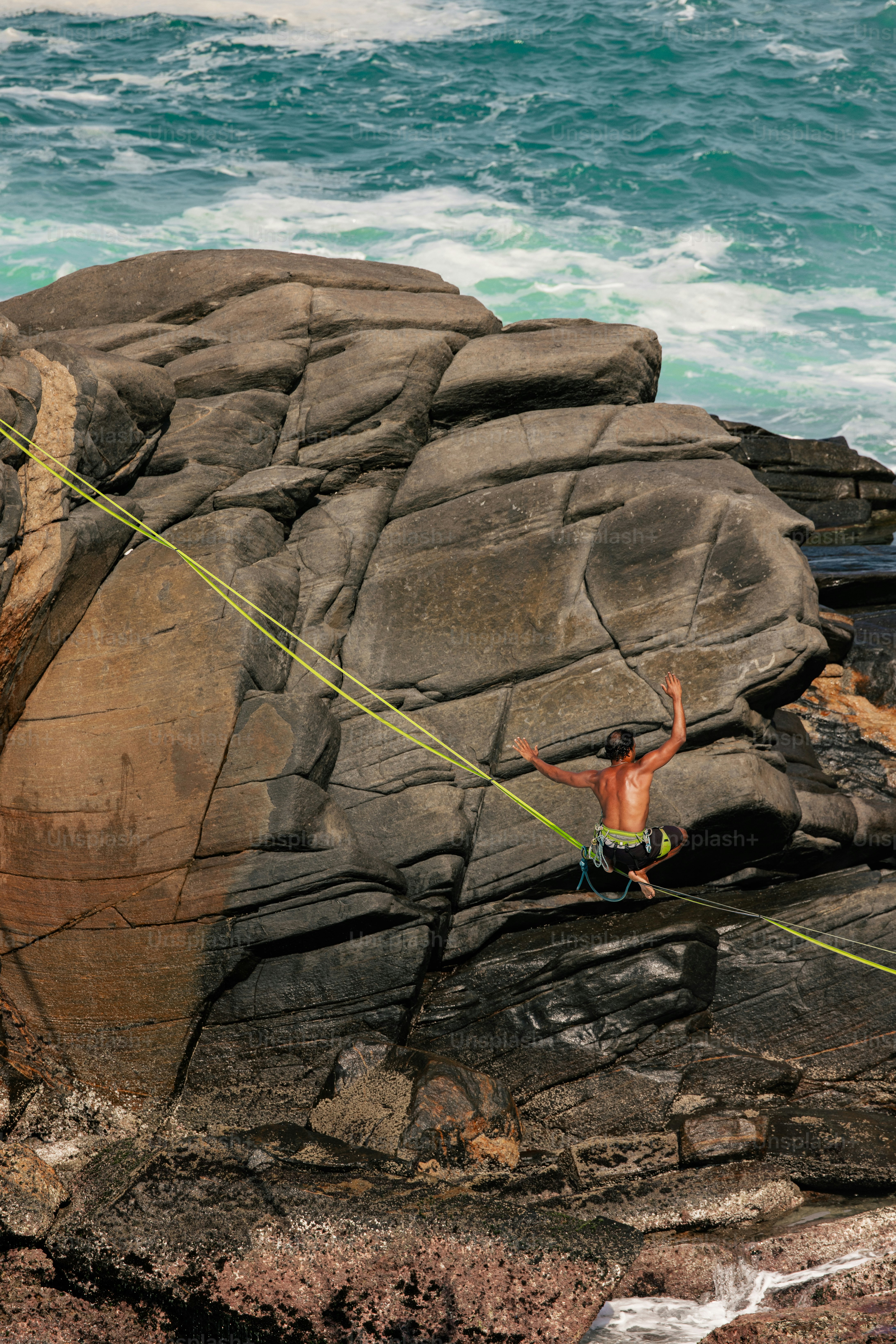 A man on a rope on the rocks by the ocean
