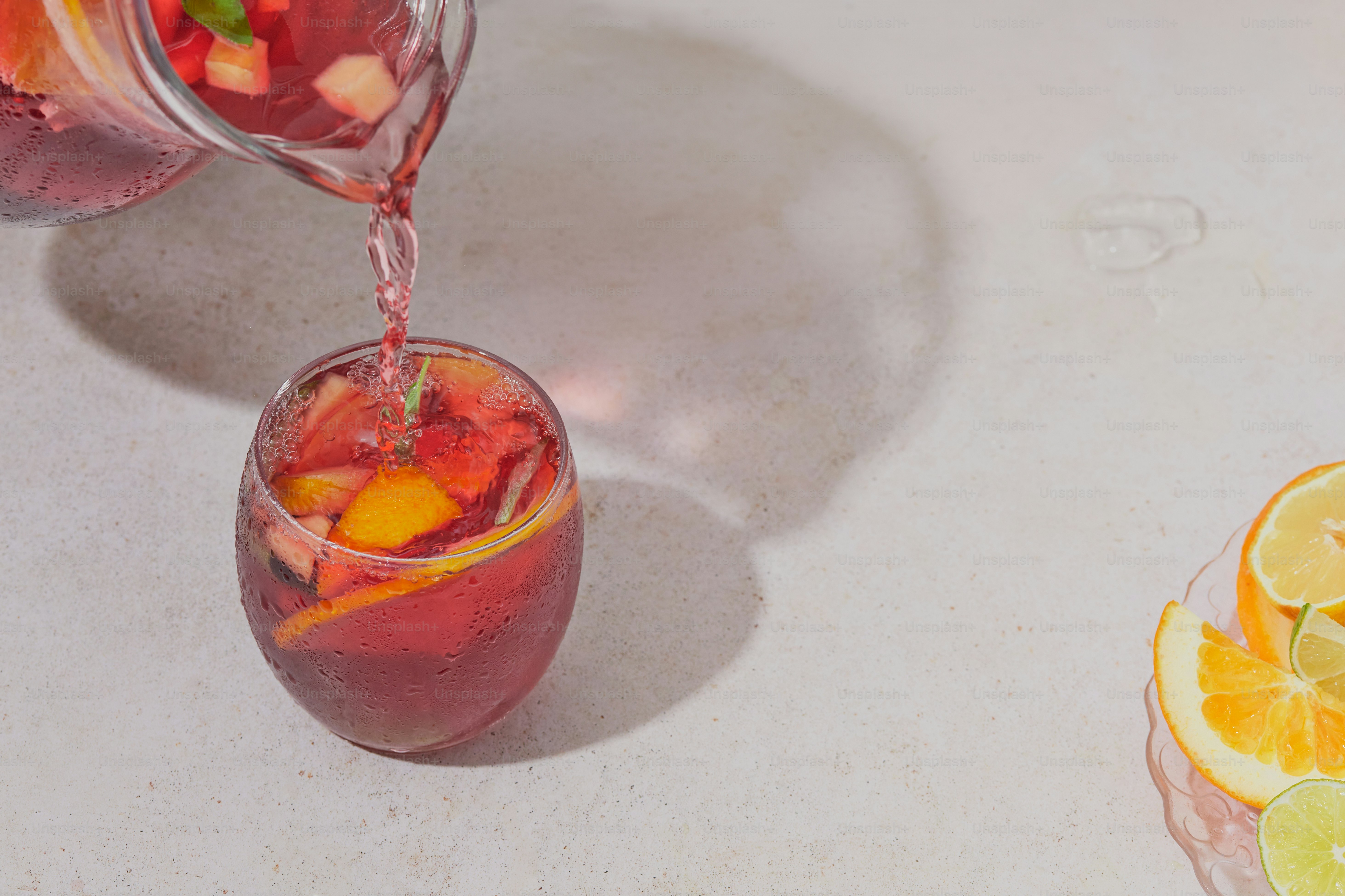 A pitcher of liquid pouring into a glass filled with fruit