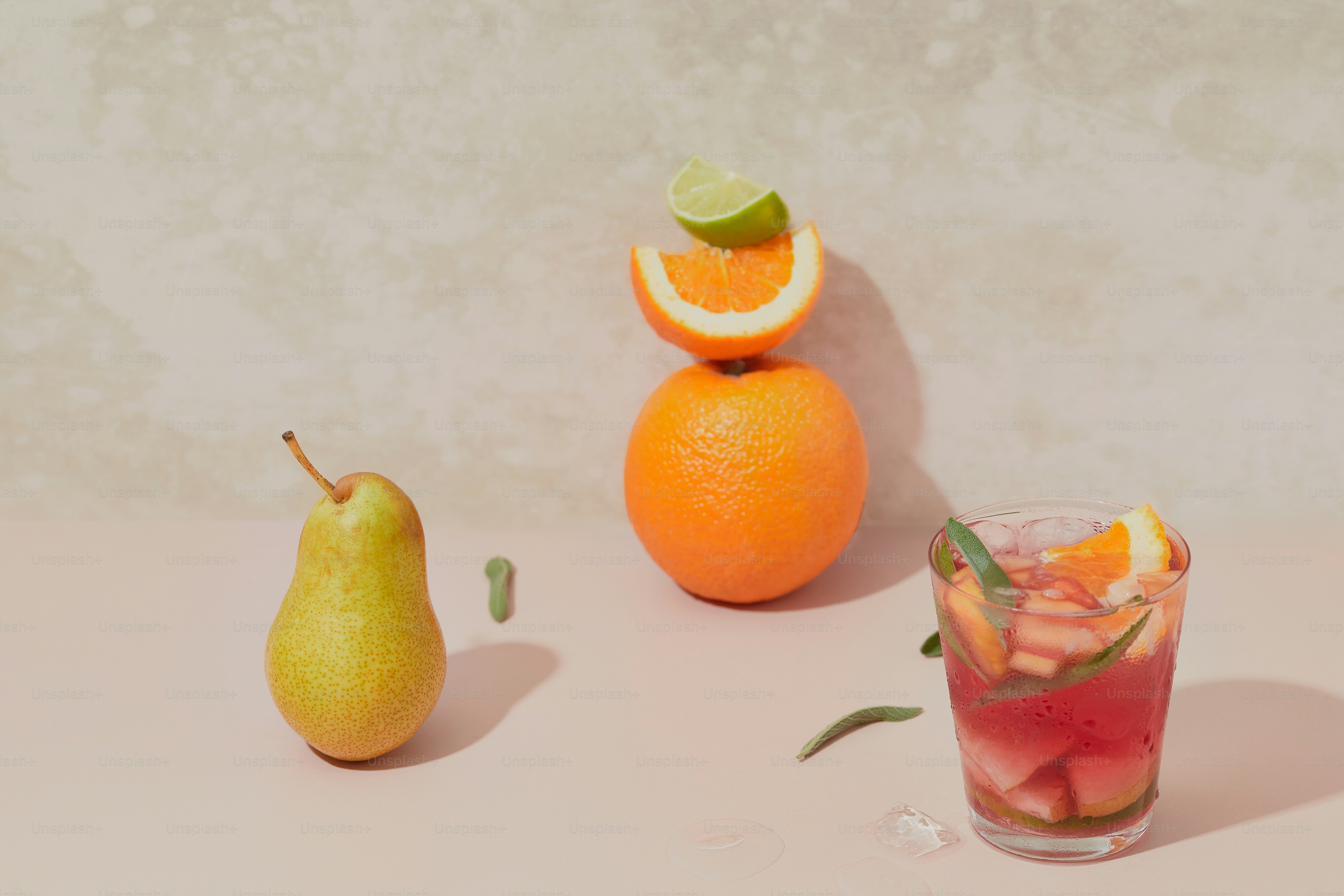 A glass filled with a drink next to two oranges and a pear