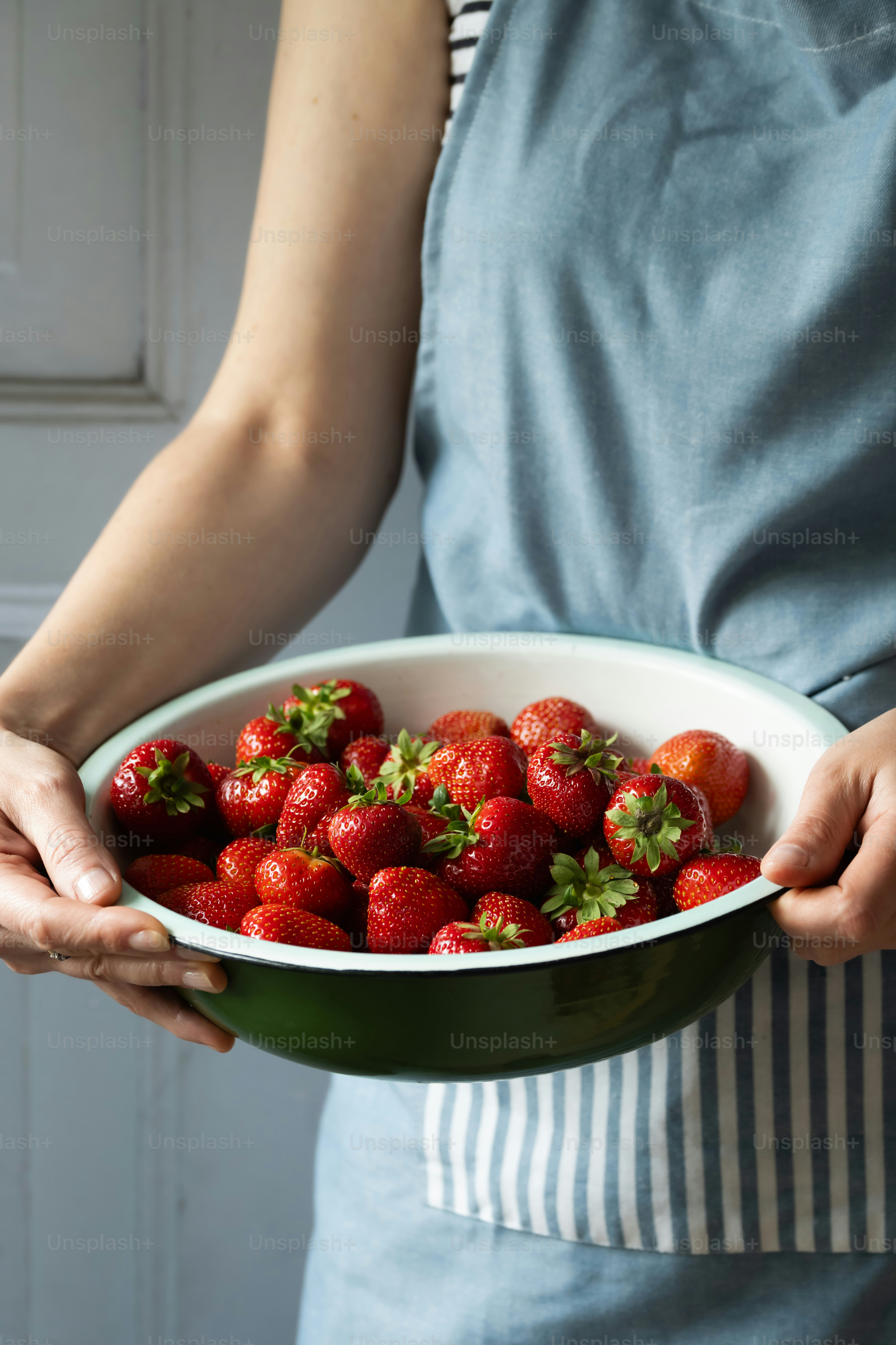 A person holding a bowl of strawberries in their hands