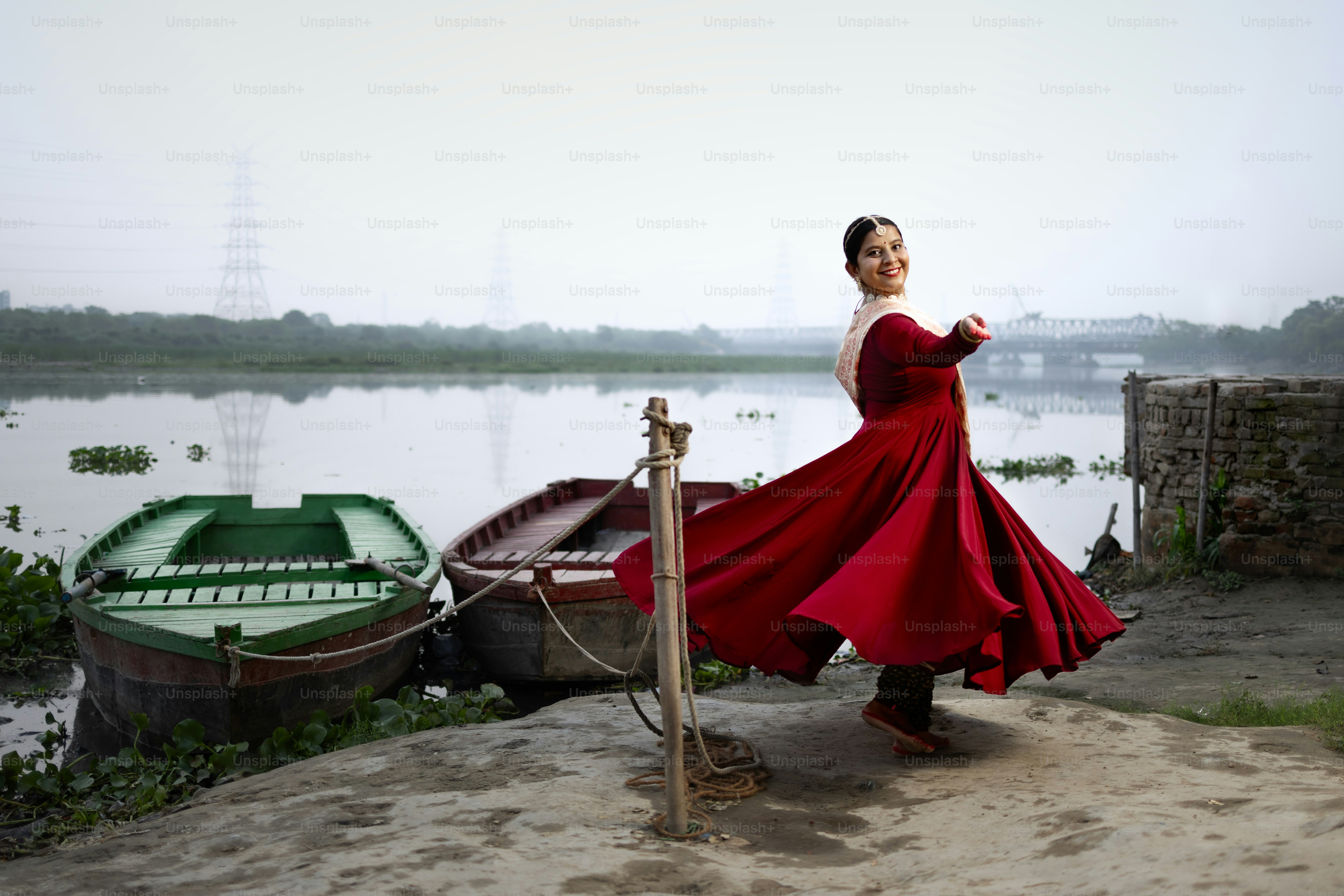A woman in a red dress standing on a beach next to boats photo – India ...