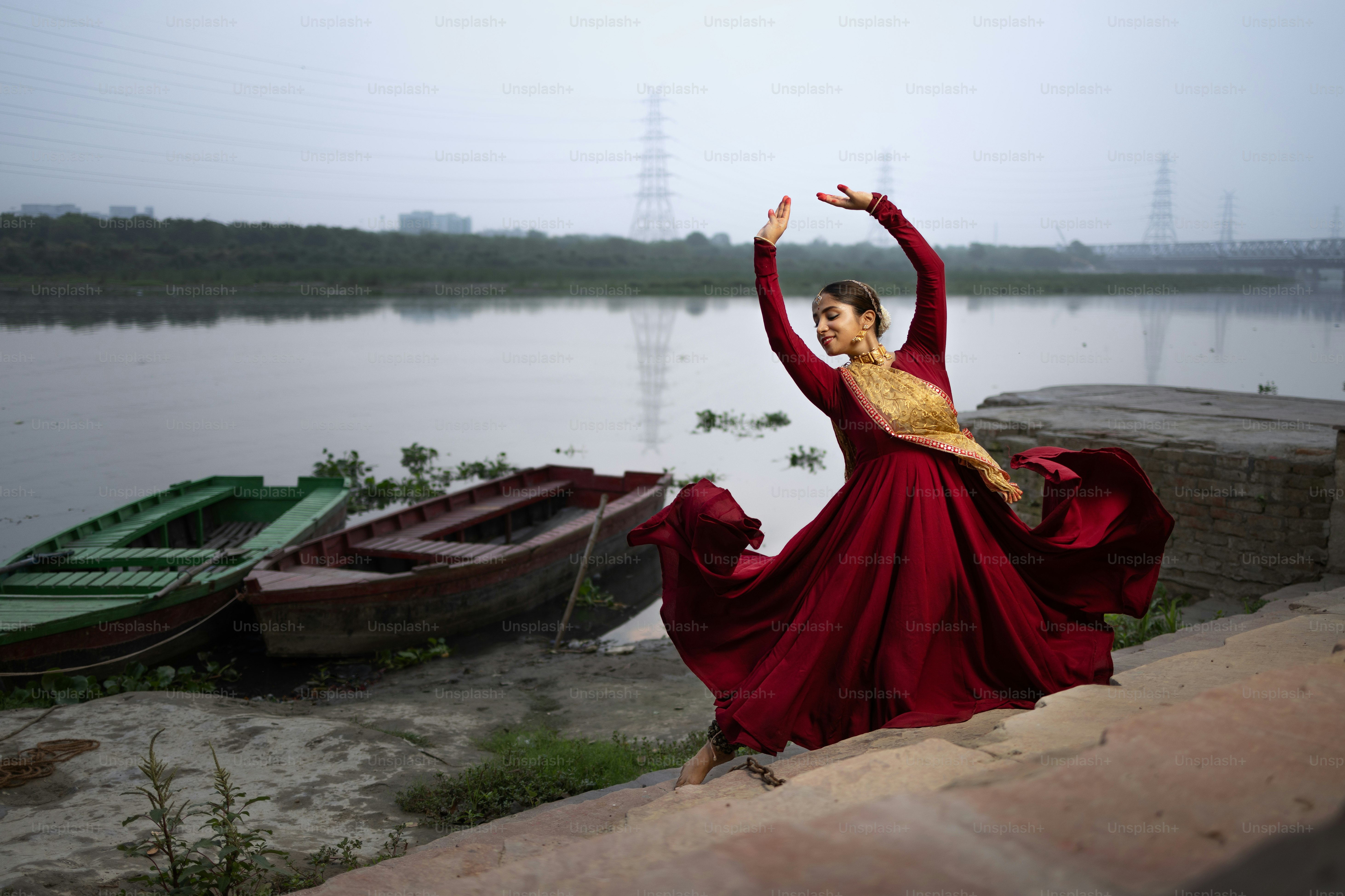 A woman in a red dress is dancing by a lake