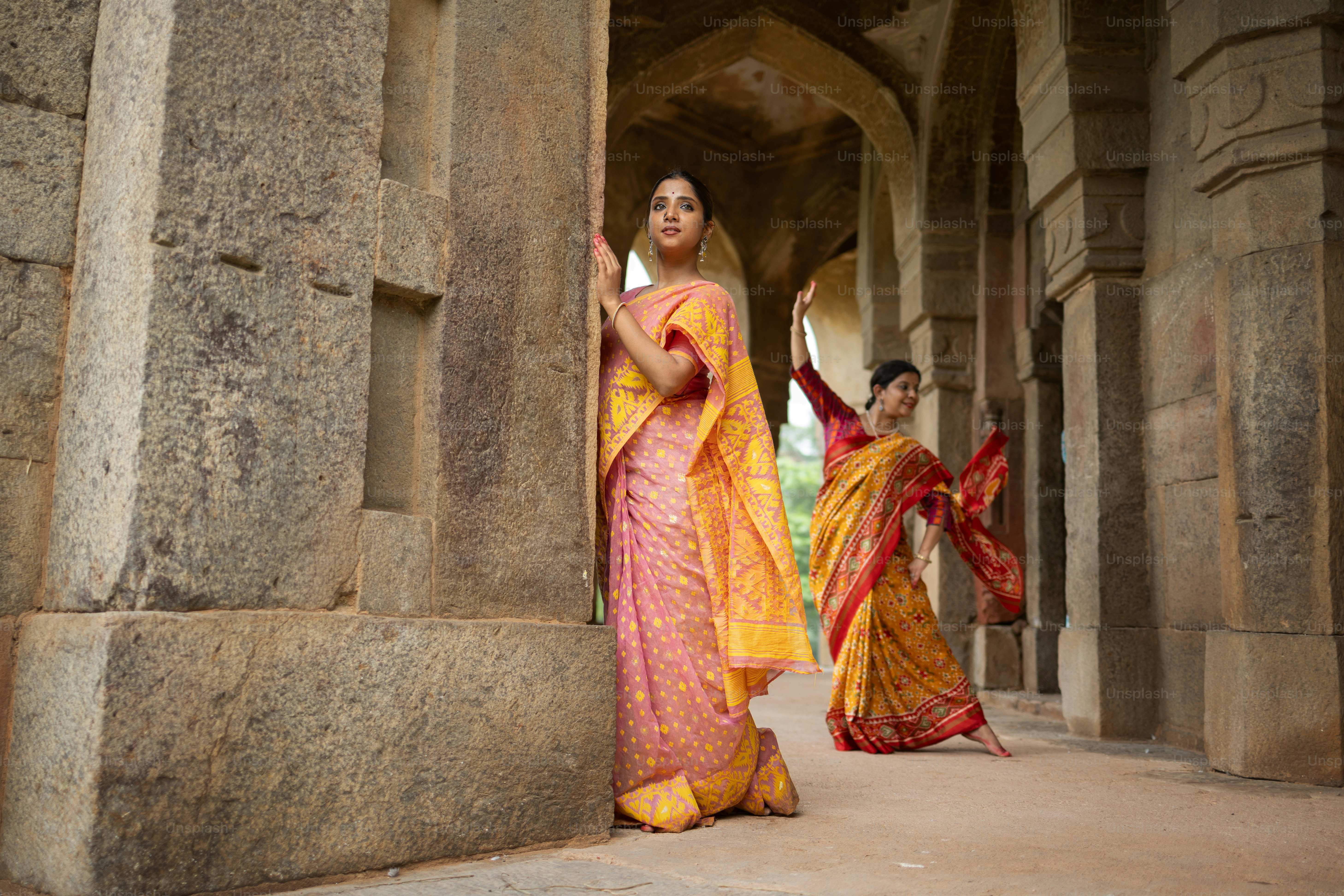 Une femme en sari jaune et rouge debout à côté d’une autre femme en