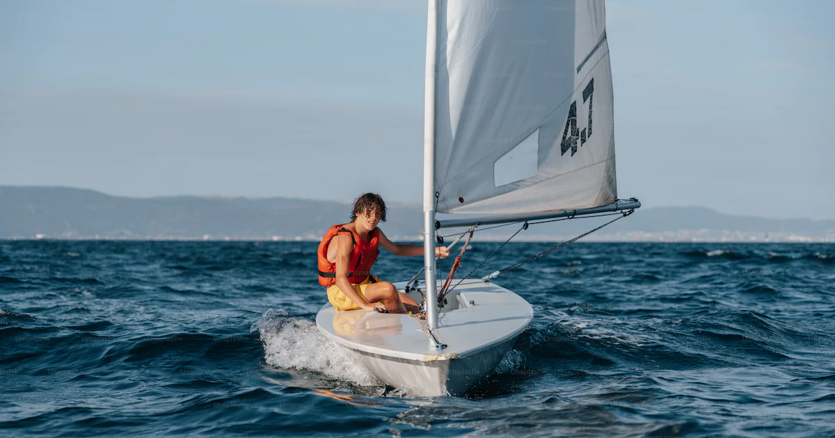 A man riding a sailboat on top of a body of water photo – Sailboat ...