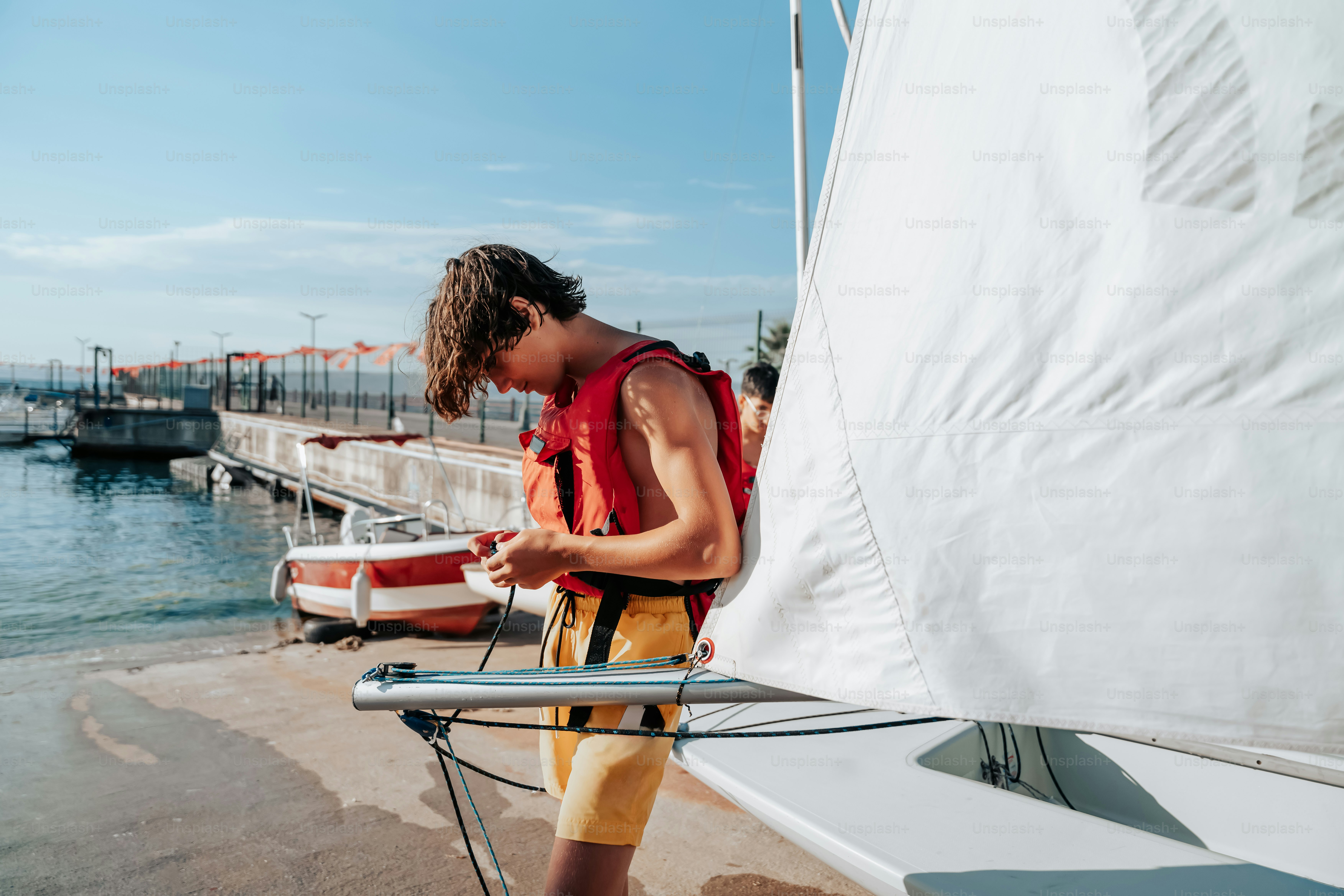 A young man standing next to a sail boat