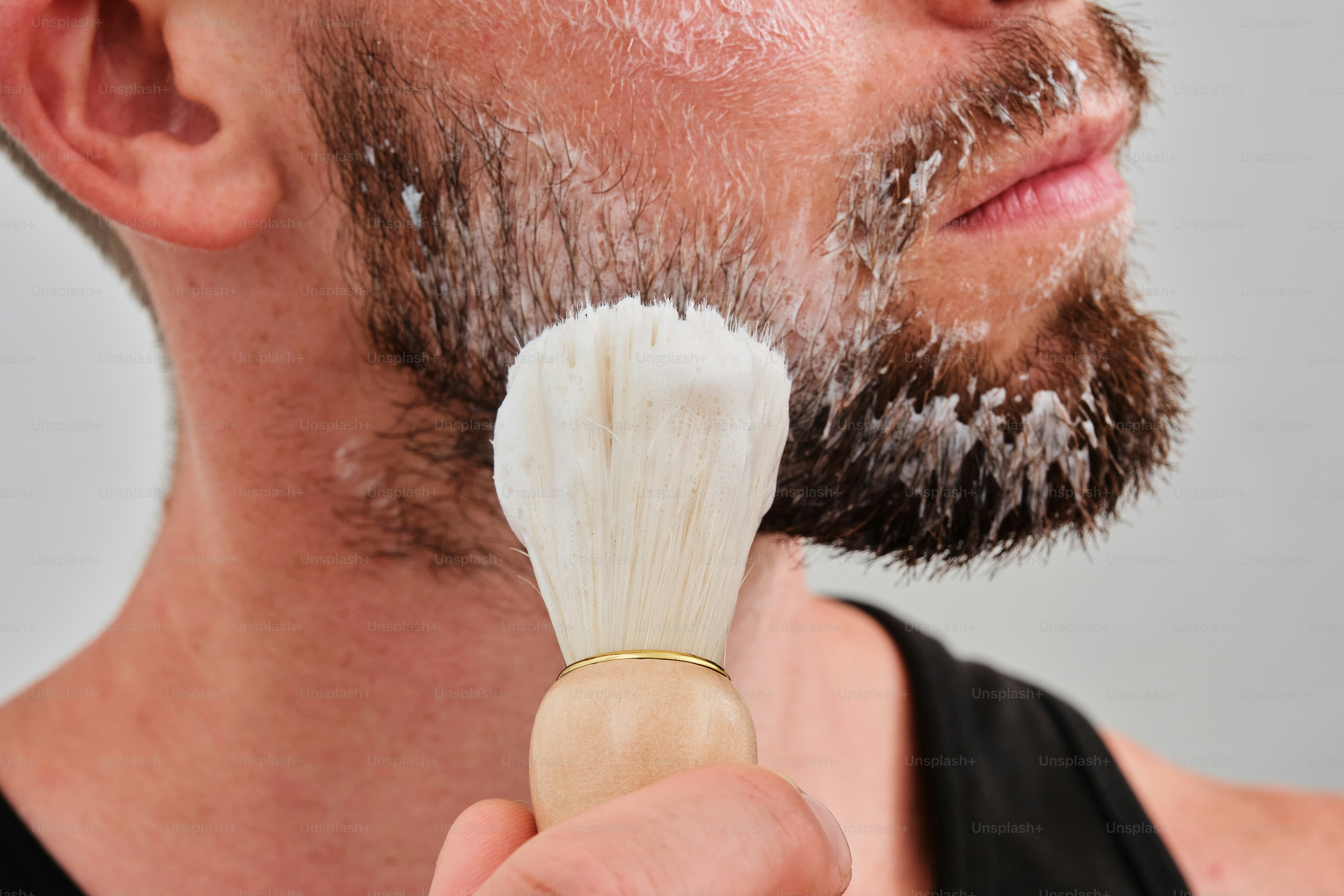 A man is shaving his face with a shaving brush