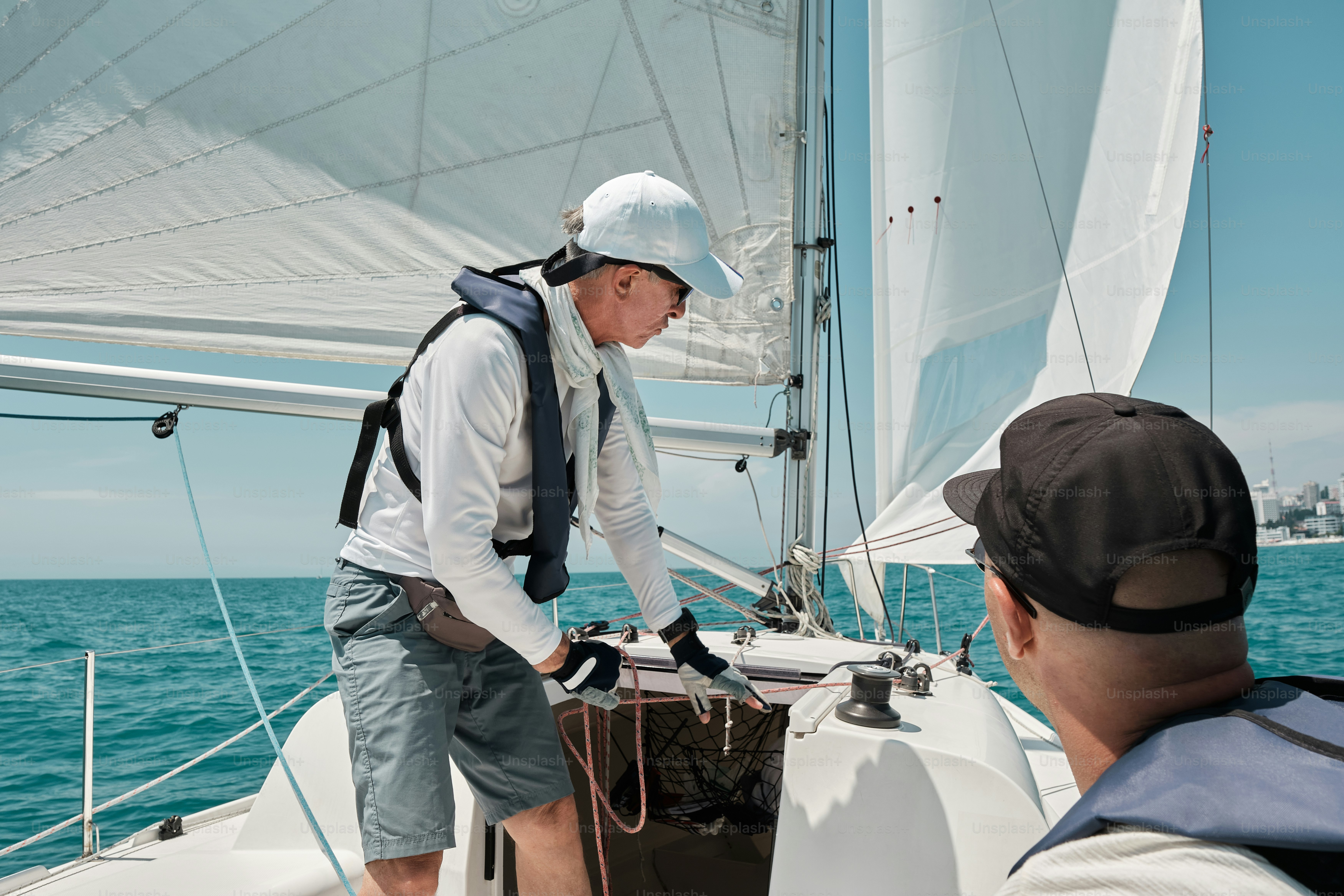 A man standing on a sailboat while another man watches