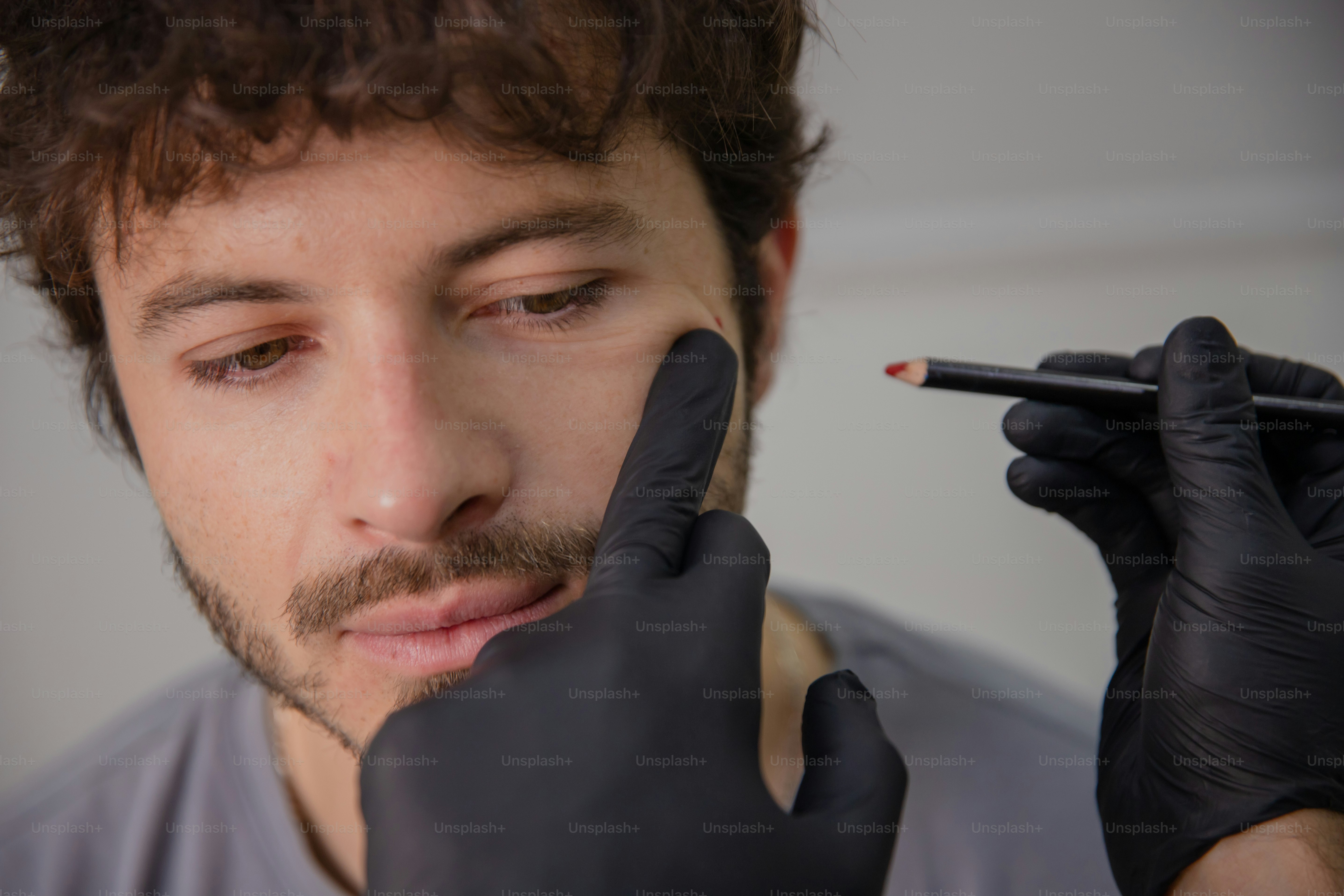 A man in a gray shirt and black gloves holding a pencil