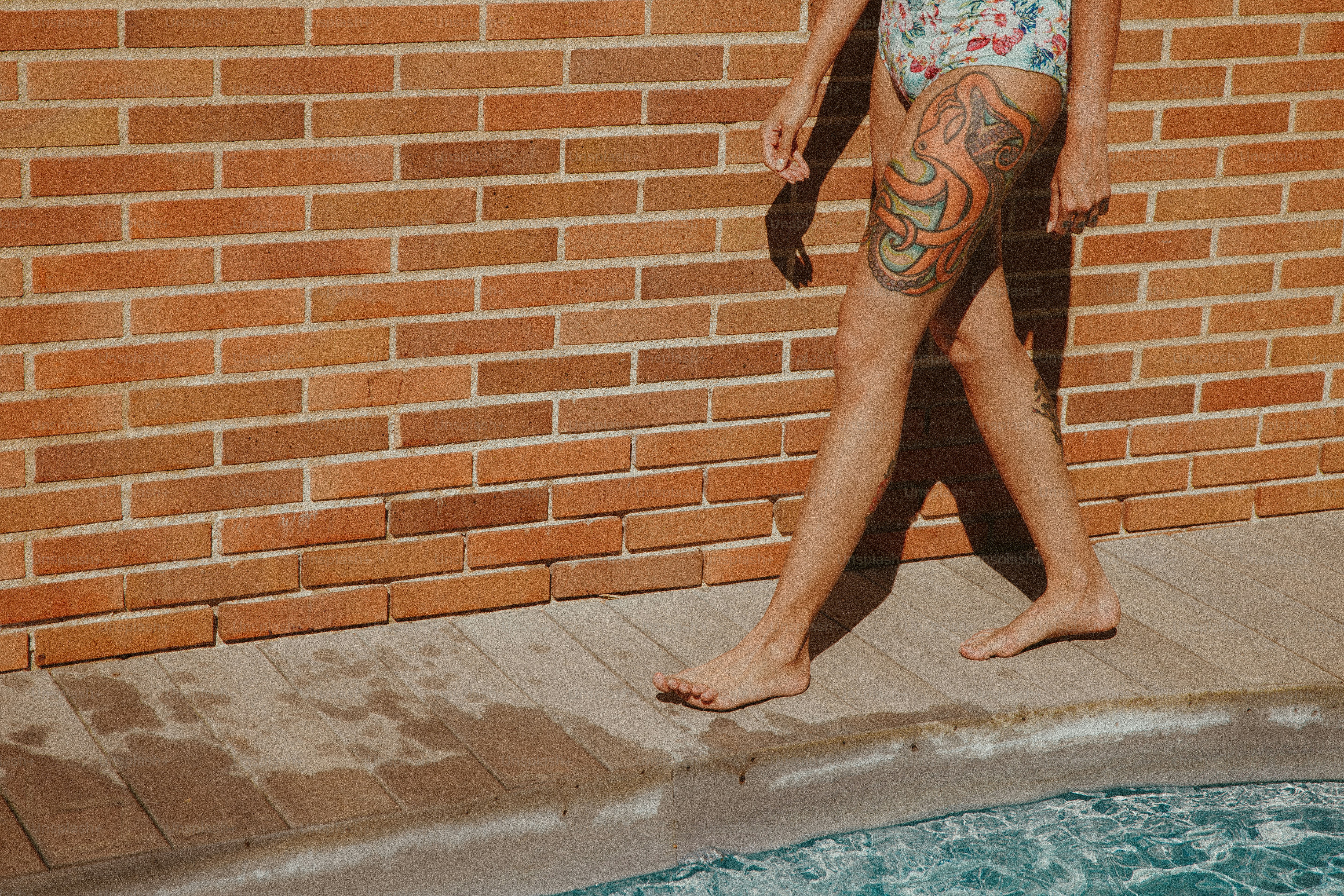 A woman standing next to a brick wall near a pool