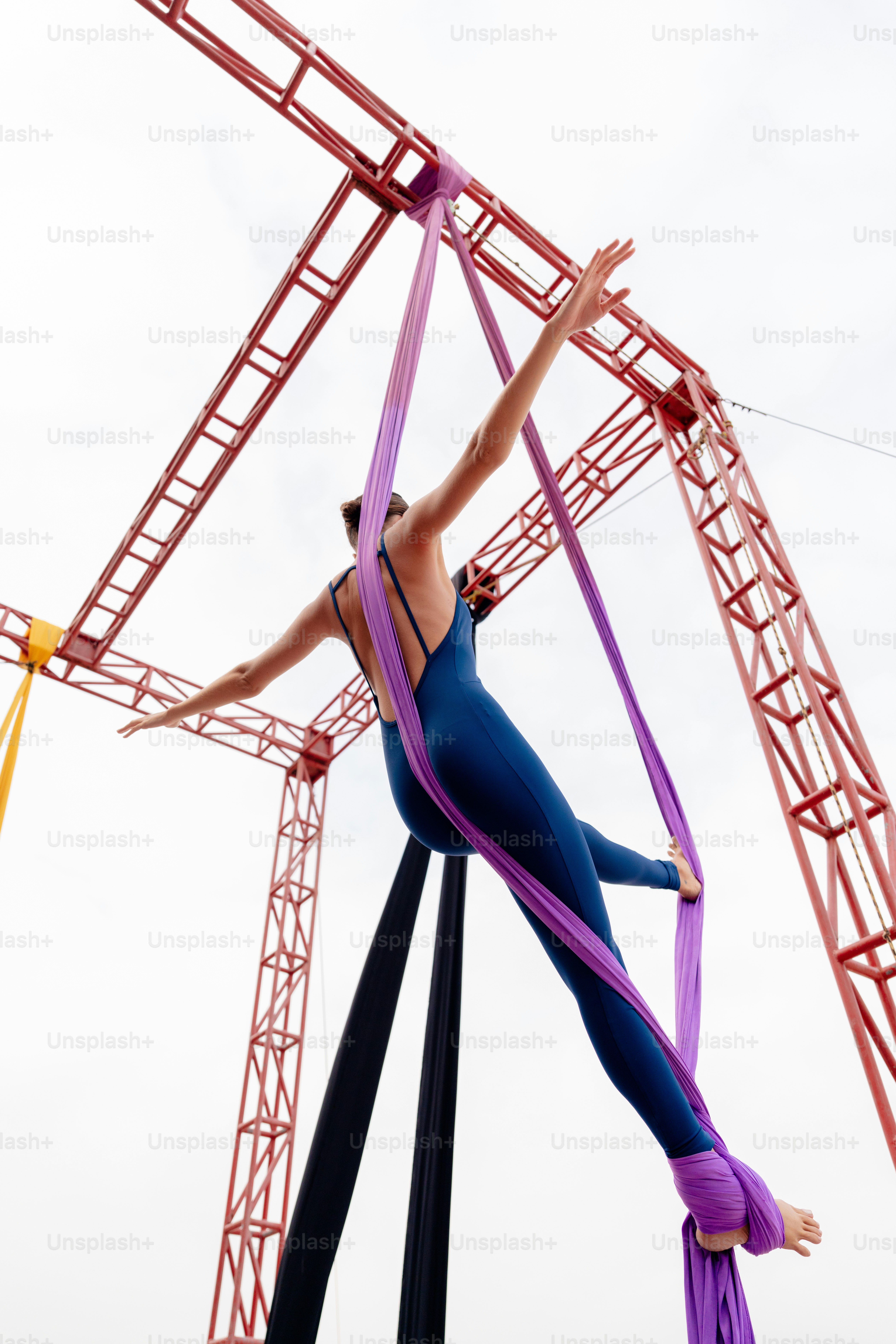 A woman is performing aerial acrobatic tricks on a pole