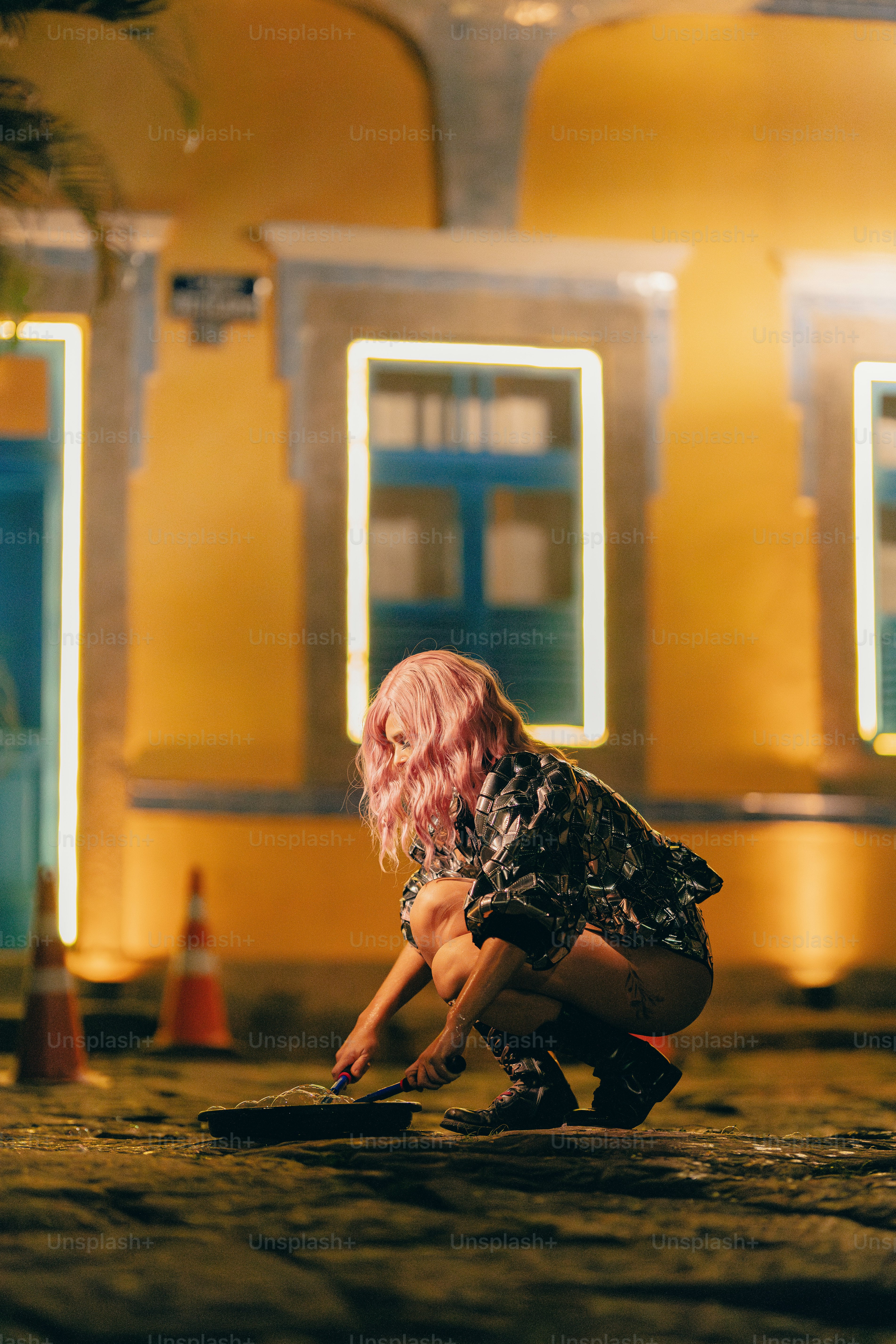 A woman with pink hair kneeling down in front of a building