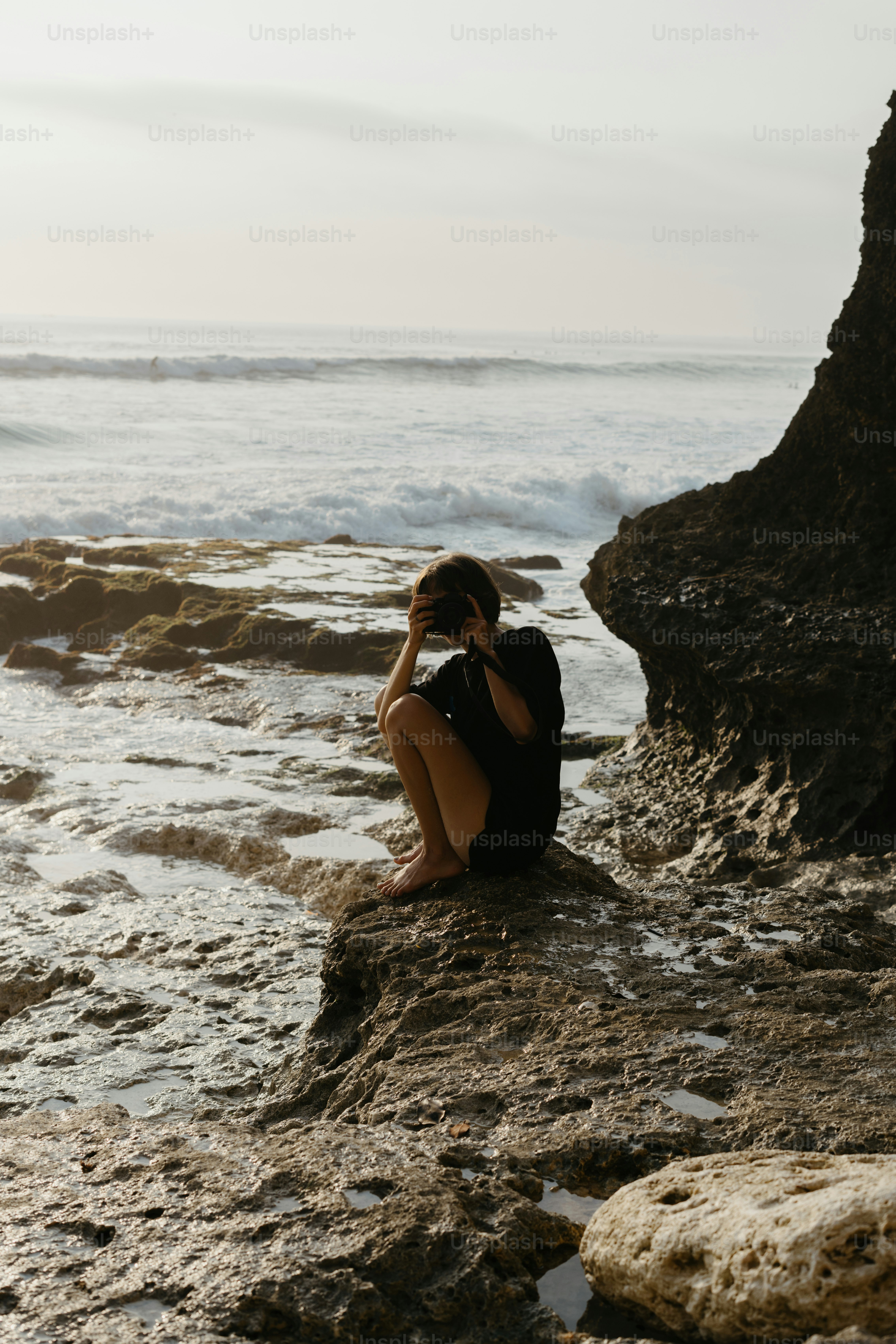 A woman sitting on top of a rock next to the ocean