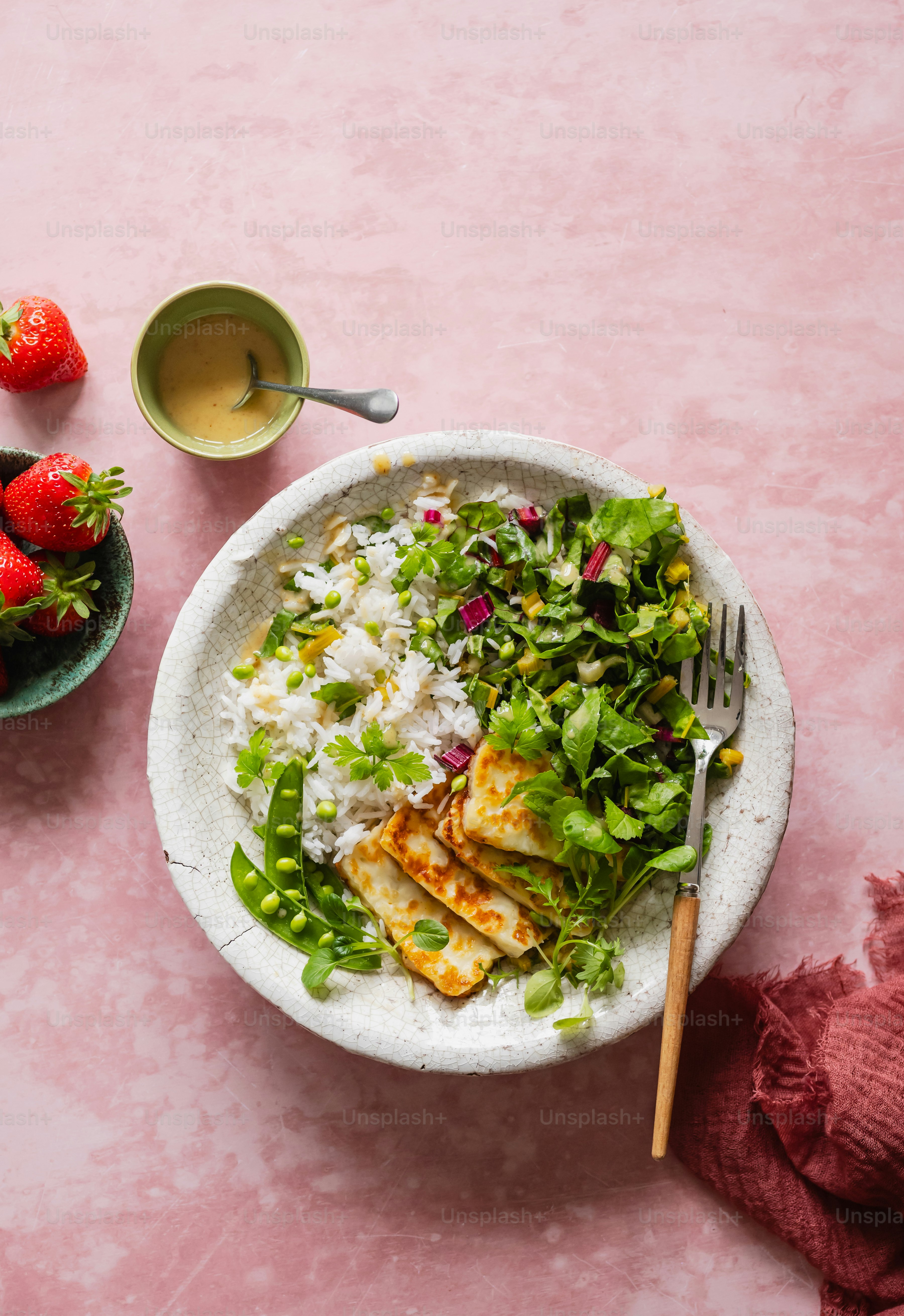 A bowl of rice, salad, and strawberries on a pink surface
