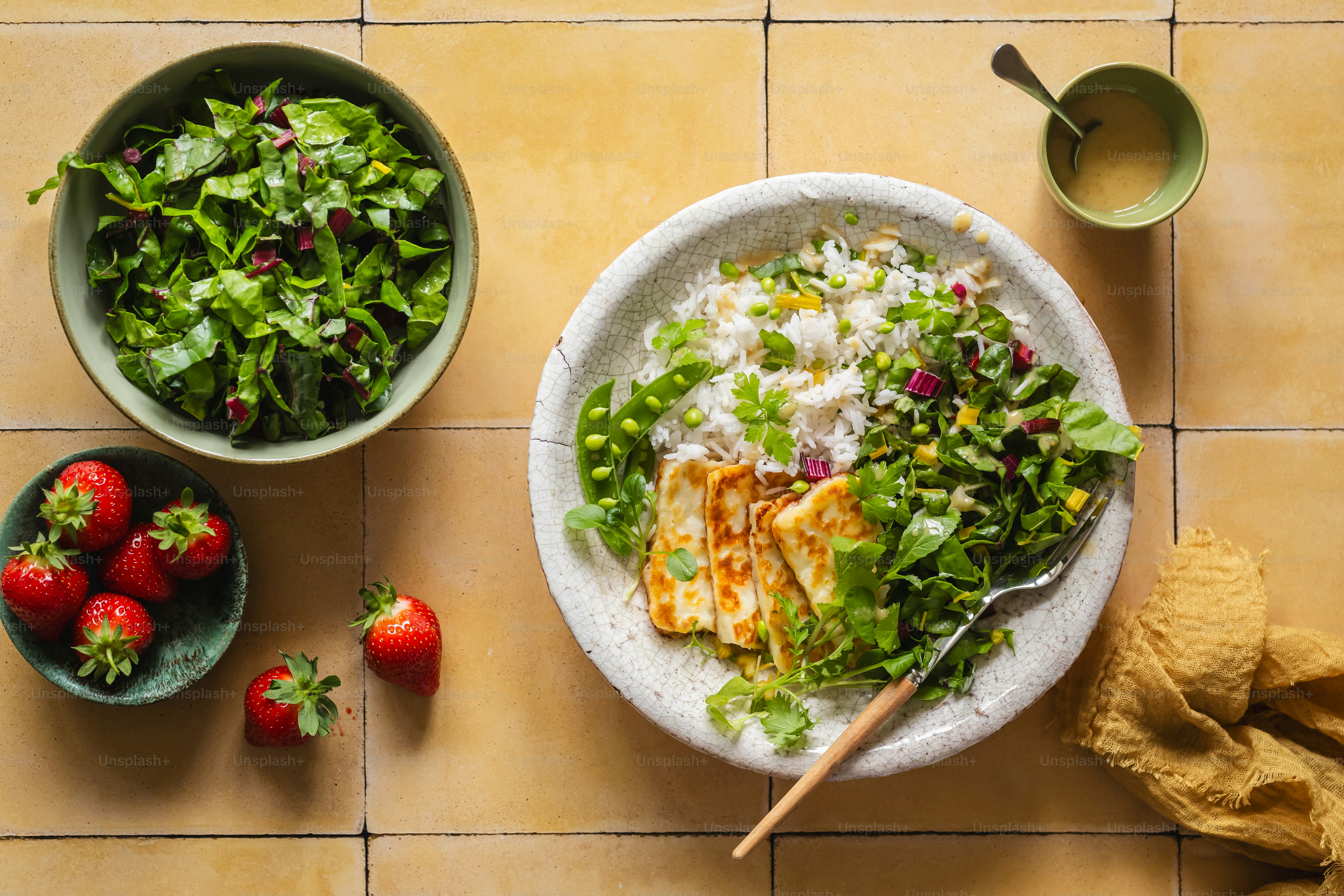A bowl of salad and a bowl of strawberries on a table
