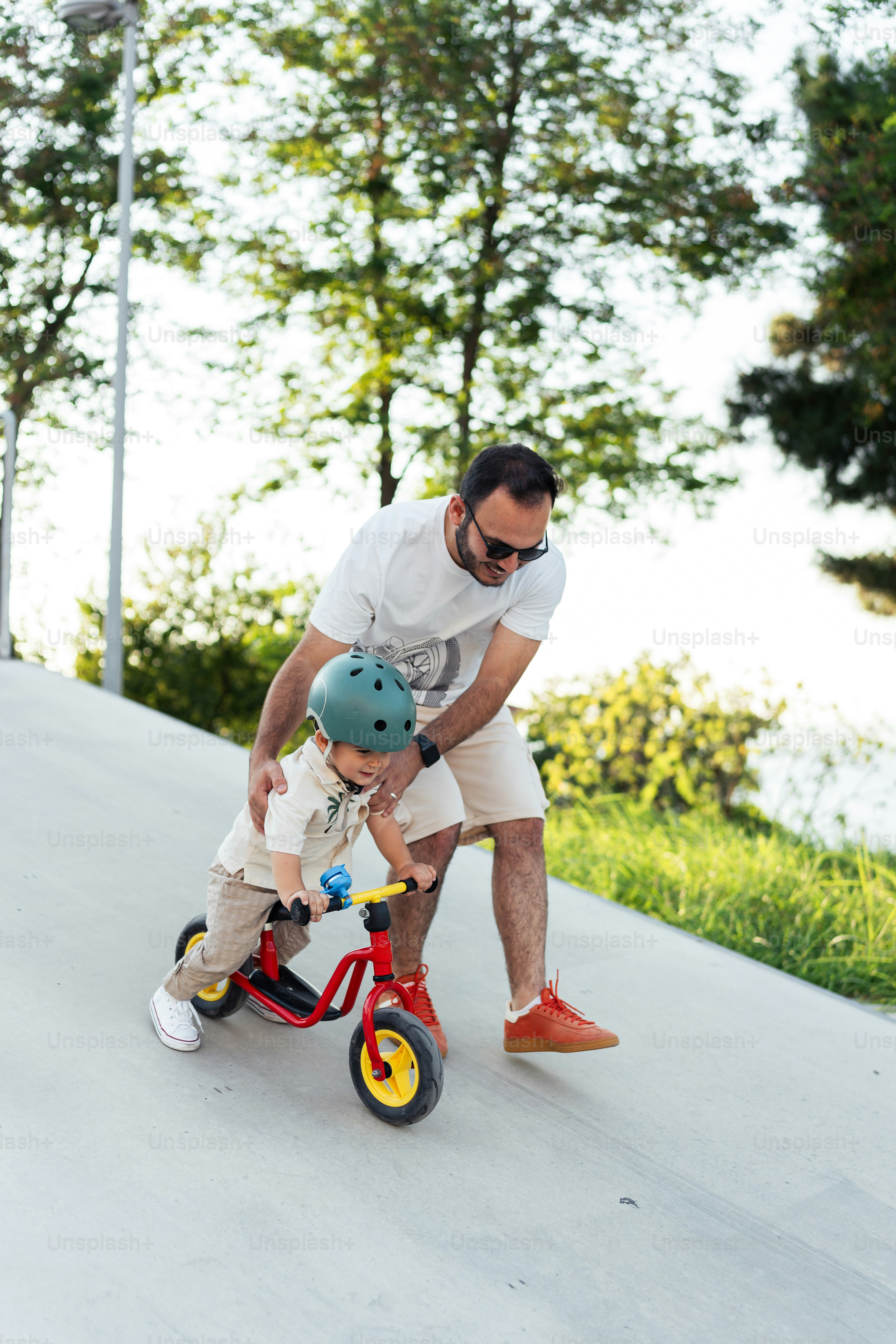 A man teaching a small boy how to ride a tricycle