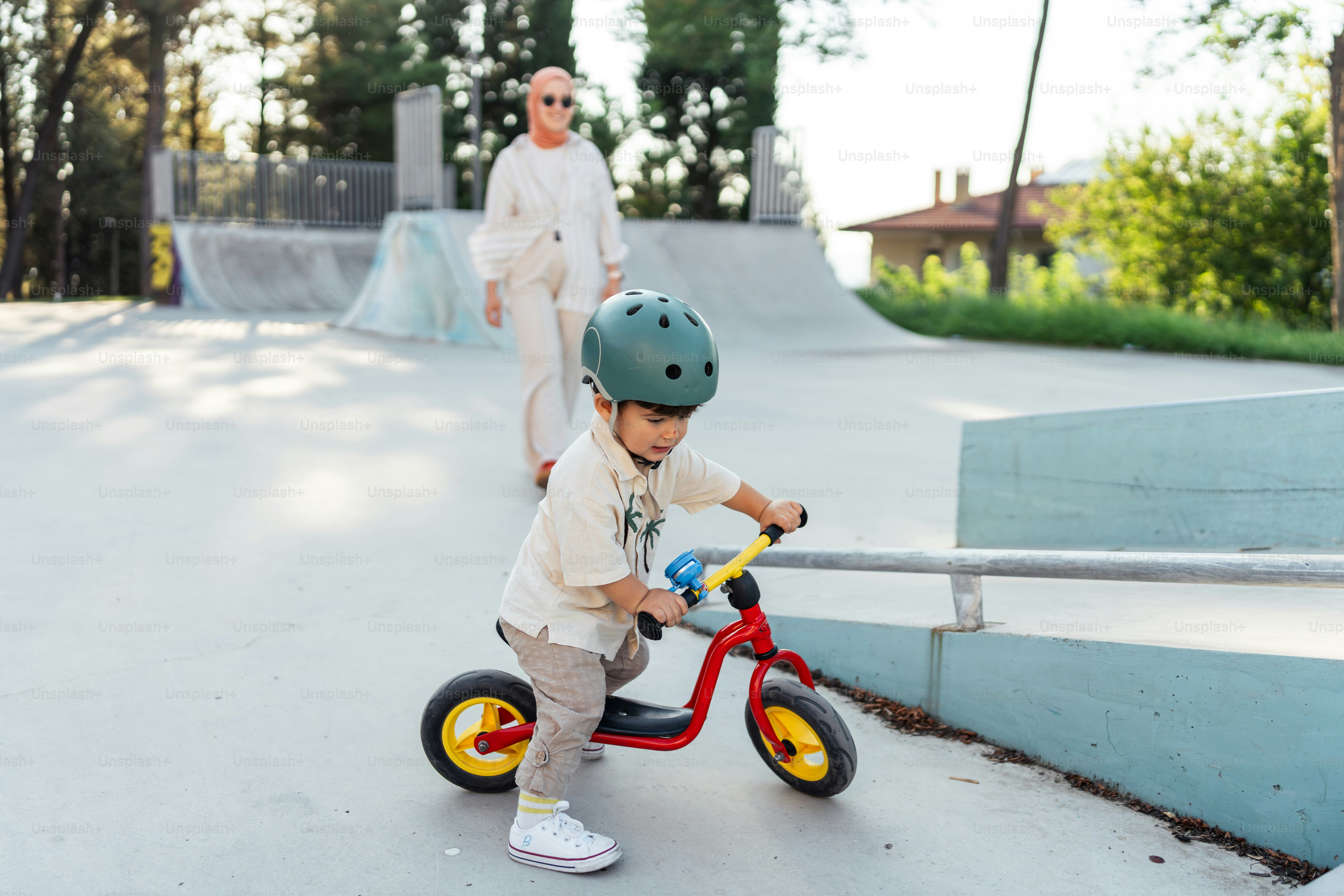 A little boy riding a red bike in a skate park