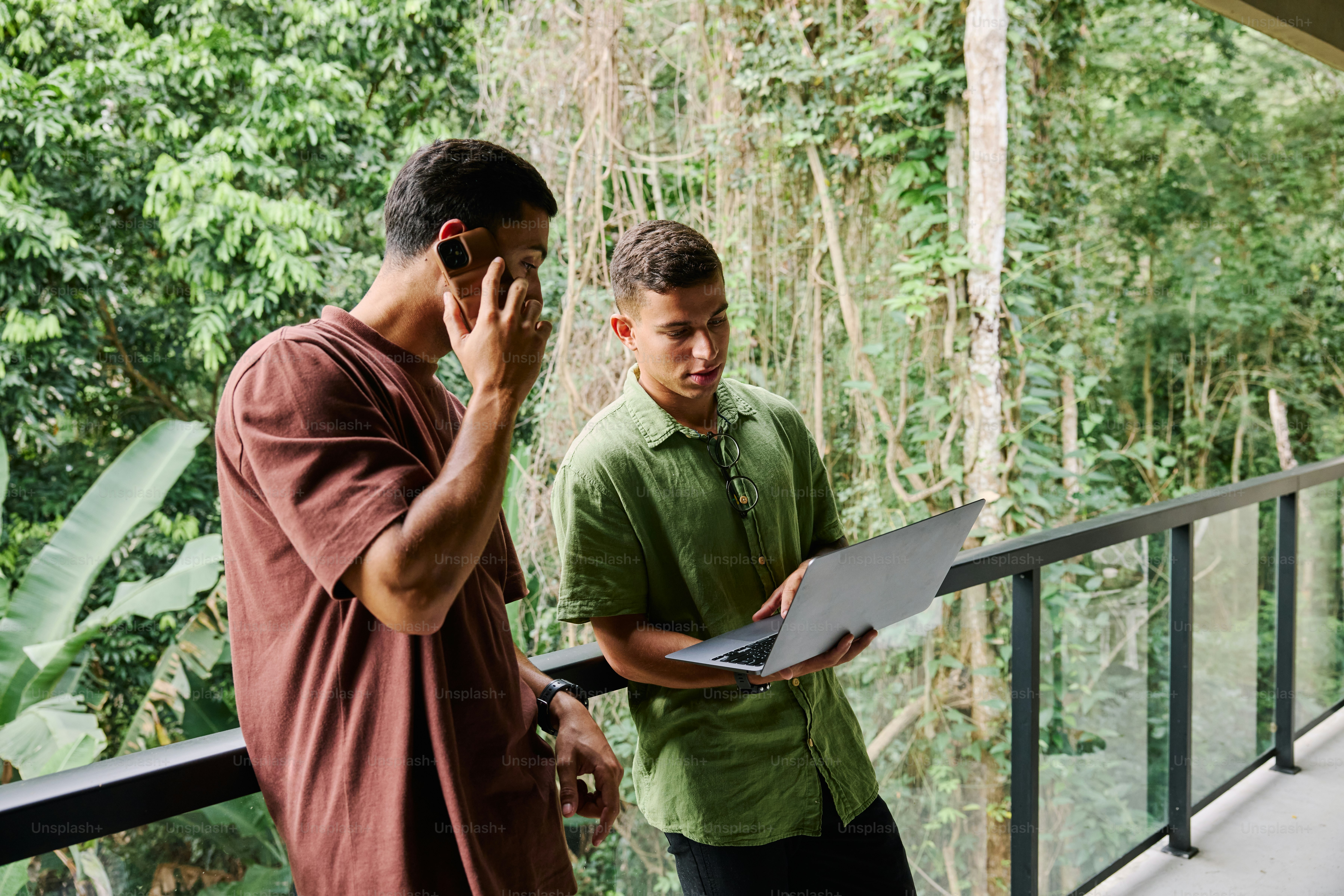 Two men standing on a balcony talking on their cell phones