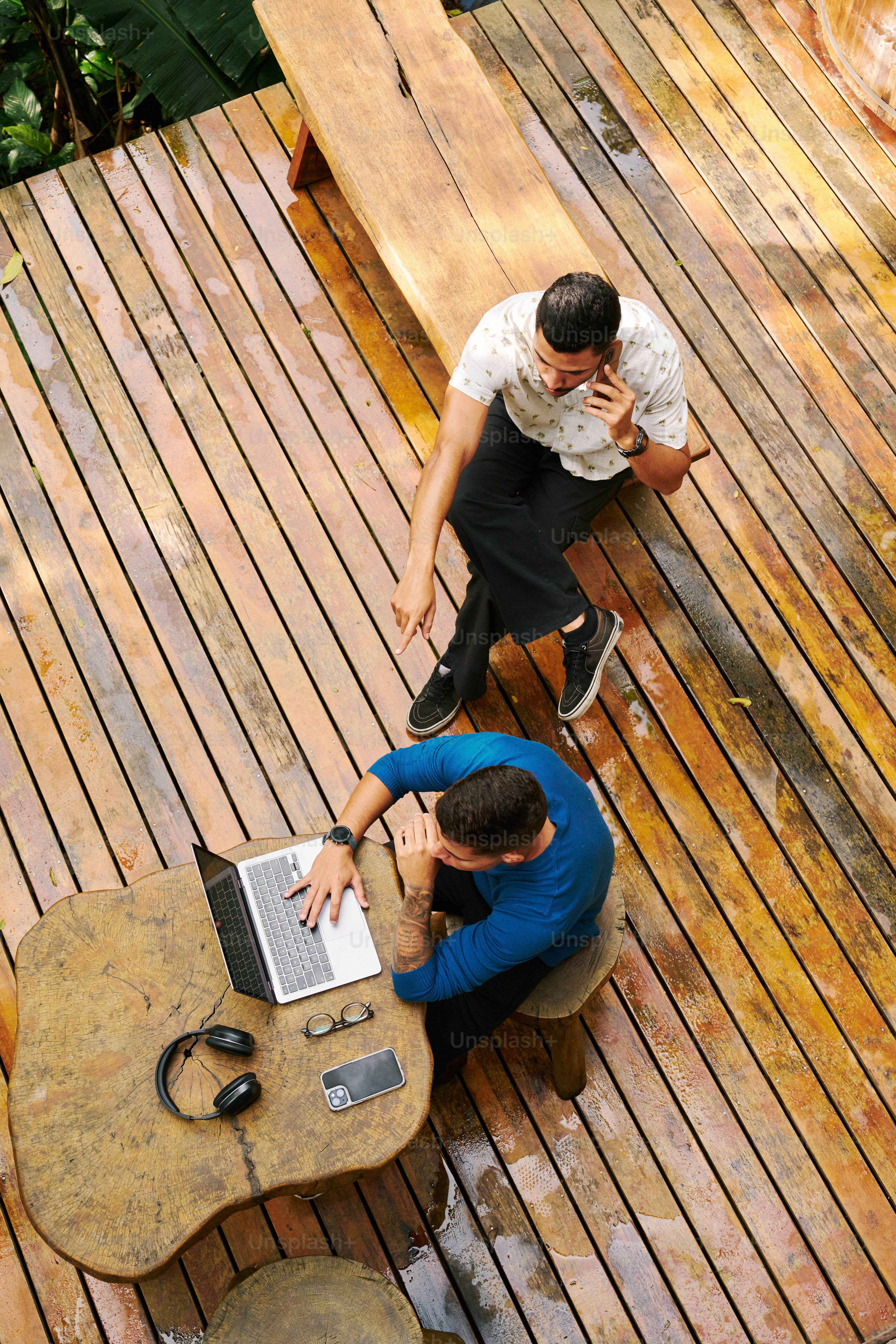 Two men sitting at a table on a wooden deck