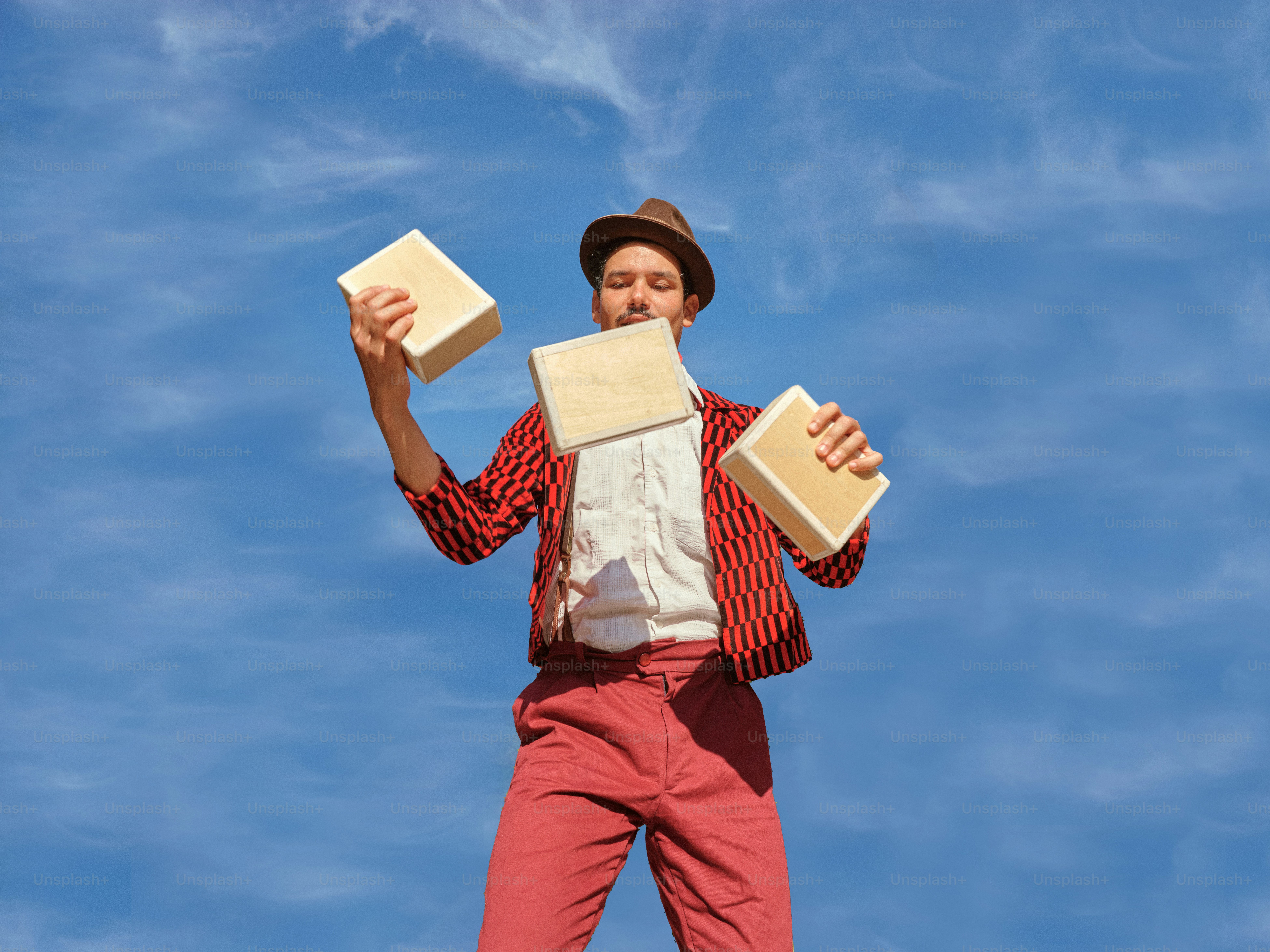 A man in red pants and a hat holding two boxes