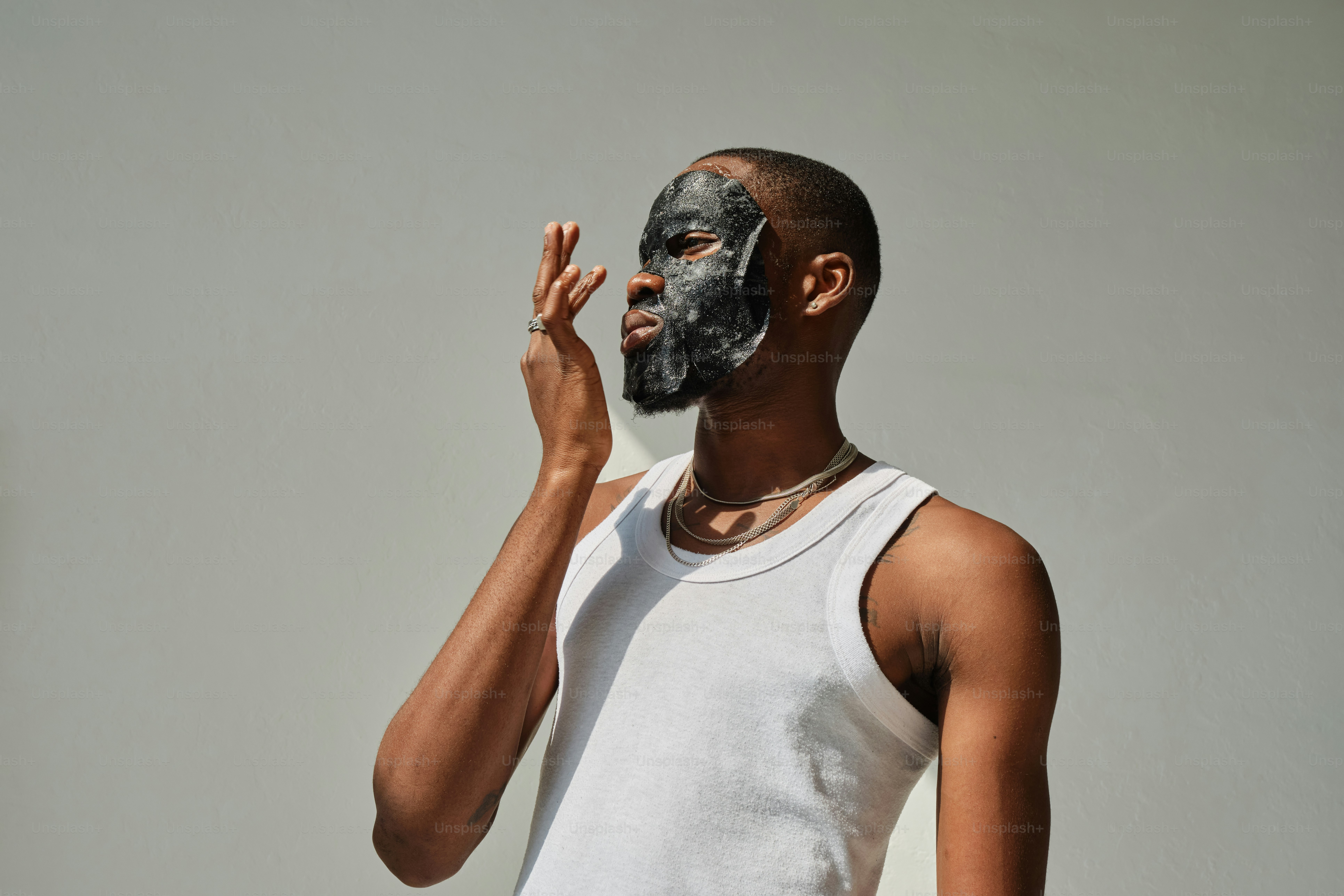 A man in a white tank top is holding his hand up to his face photo ...