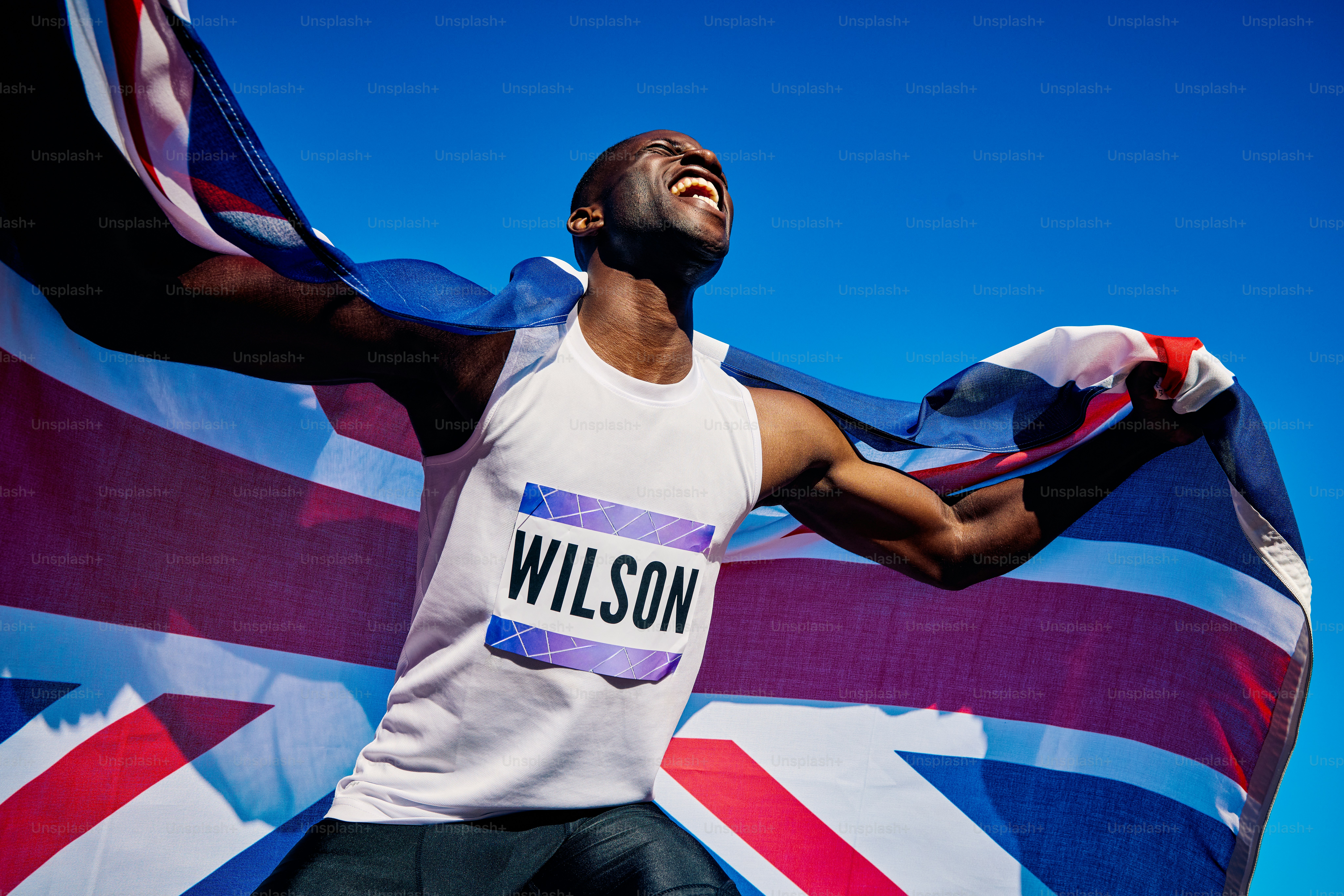 Atlet yang gembira dengan bendera Union Jack berteriak dalam kemenangan. Potret perayaan luar ruangan dengan langit biru. Konsep kemenangan dan kebanggaan nasional.