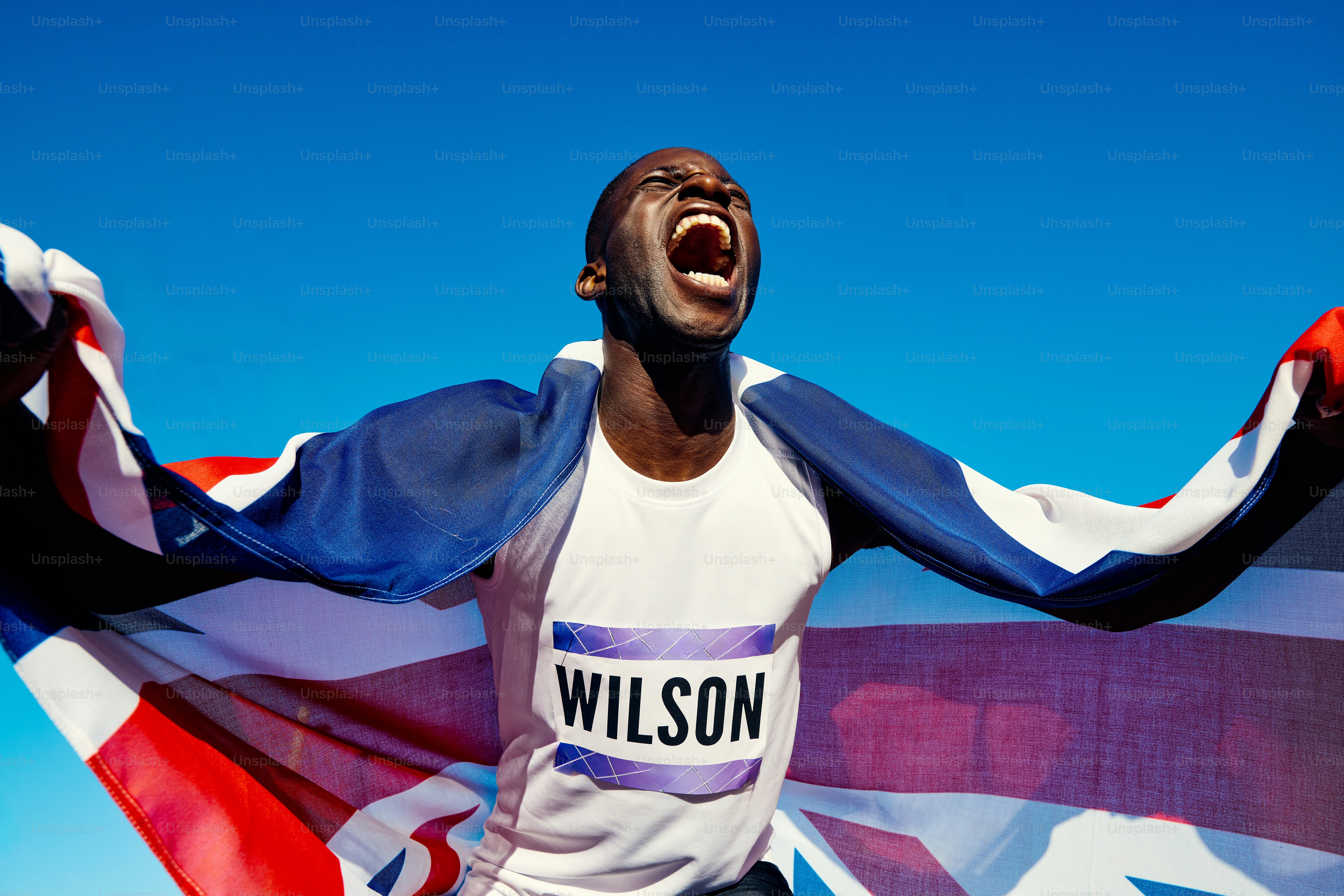 Atlet yang gembira dengan bendera Union Jack berteriak dalam kemenangan. Potret perayaan luar ruangan dengan langit biru. Konsep kemenangan dan kebanggaan nasional.