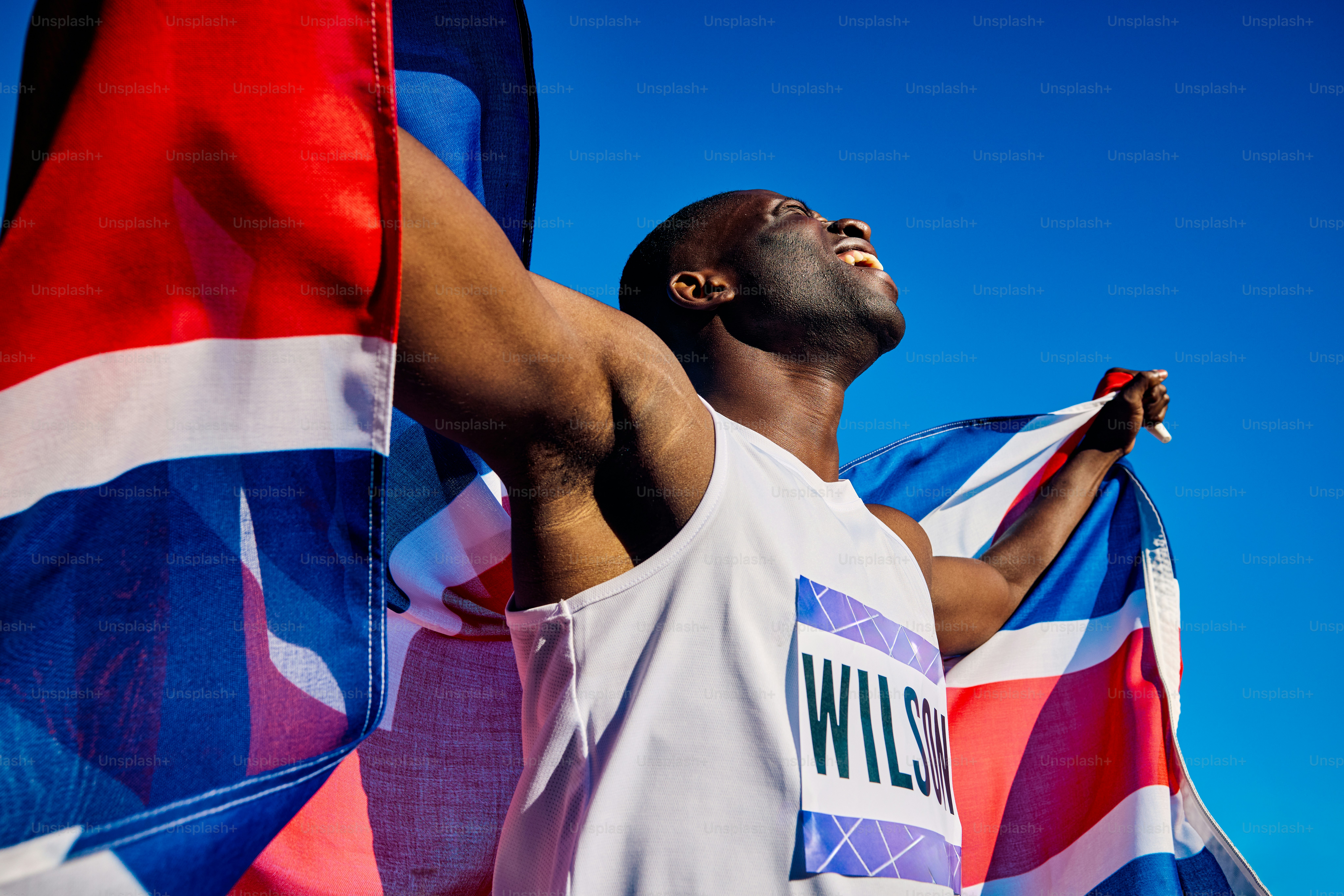 Atlet yang gembira dengan bendera Union Jack berteriak dalam kemenangan. Potret perayaan luar ruangan dengan langit biru. Konsep kemenangan dan kebanggaan nasional.