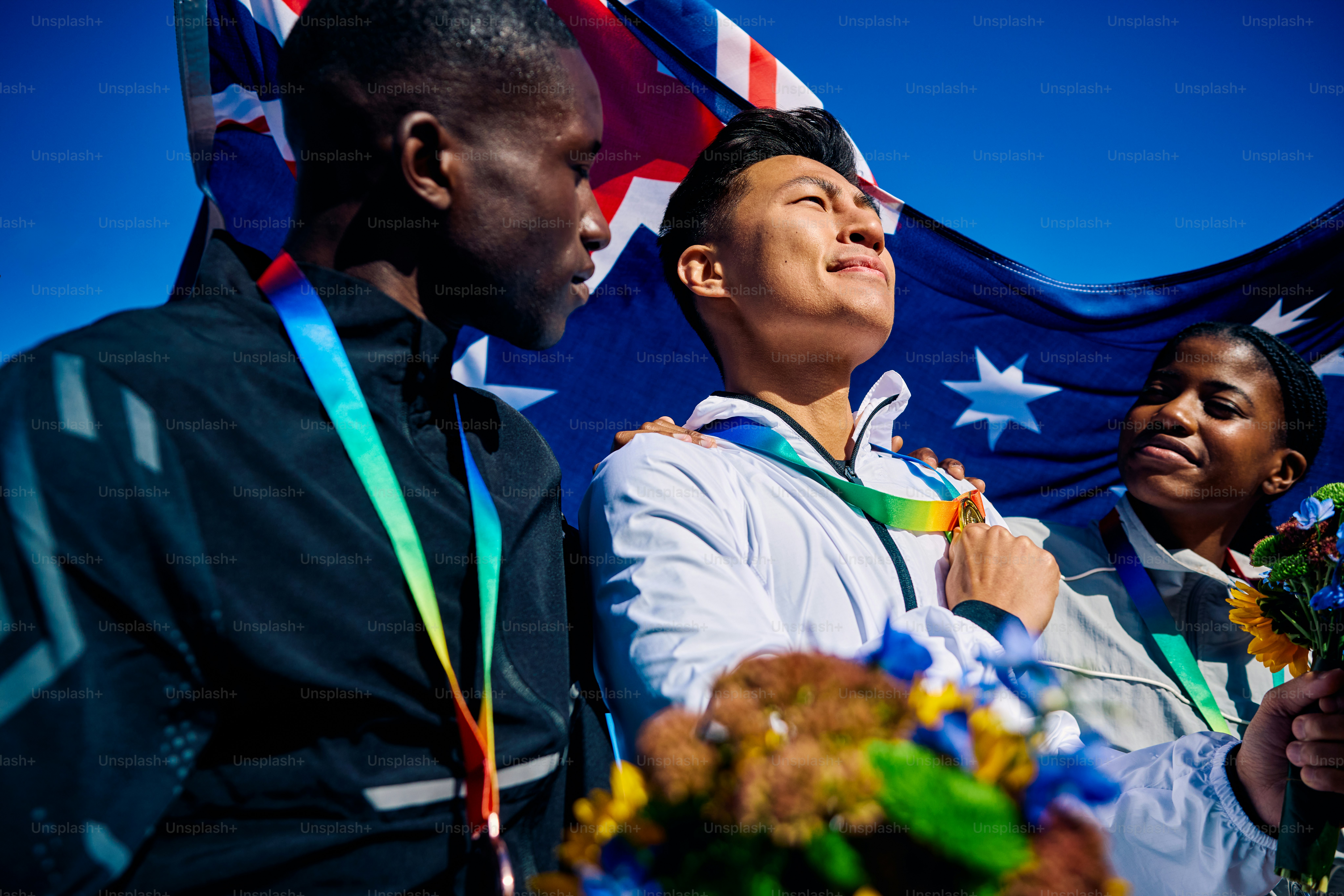 Atlet Australia yang gembira dengan medali dan karangan bunga di atas bendera Australia. Potret perayaan kelompok yang menyenangkan. Semangat tim dan konsep persatuan internasional.