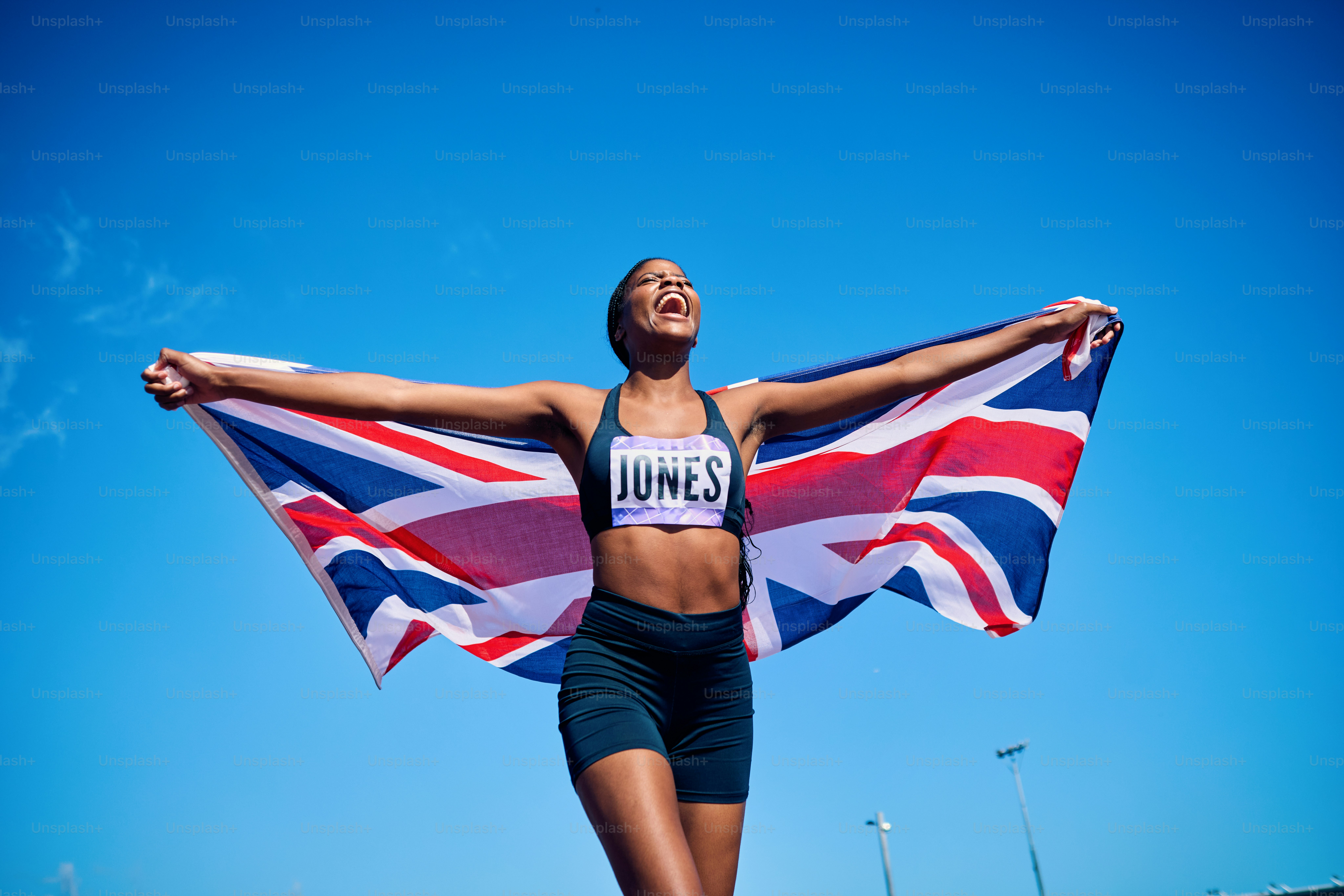 International athlete with raised arms holding the Union Jack flag. Outdoor celebration portrait with open sky. National pride and freedom concept.